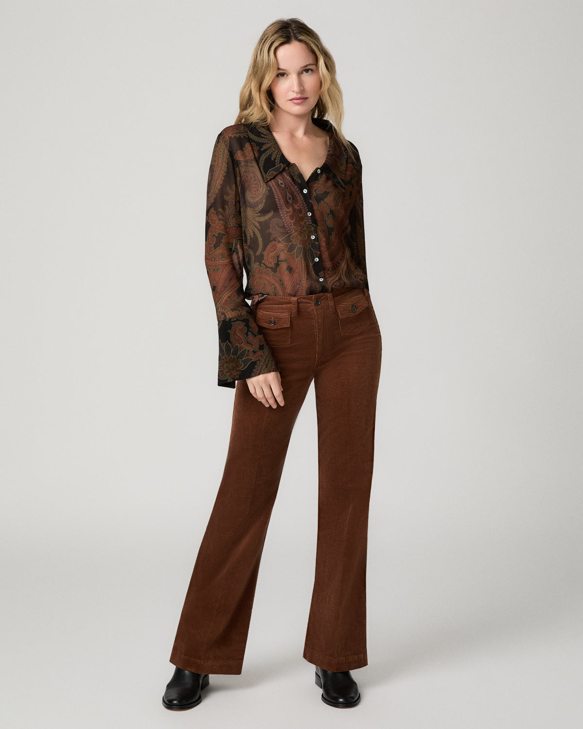 Full-length front view of a woman wearing the black and brown paisley-print Rosalinda Blouse tucked into brown flared pants with black boots.