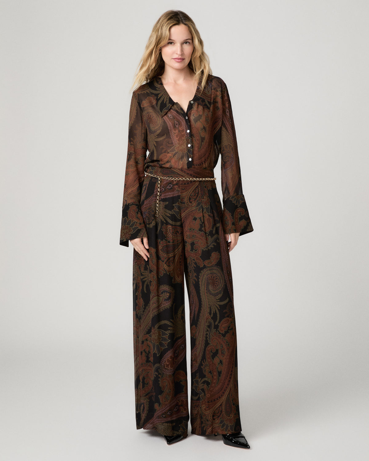 Full-length front view of a woman wearing the black and brown paisley-print Rosalinda Blouse tucked into matching wide-leg paisley pants with a smocked waistband.