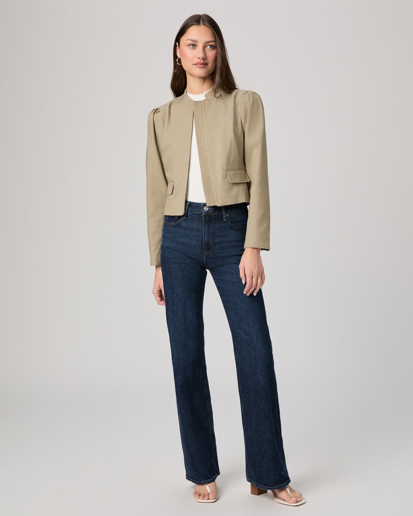Woman wearing a beige jacket and blue jeans on a gray background
