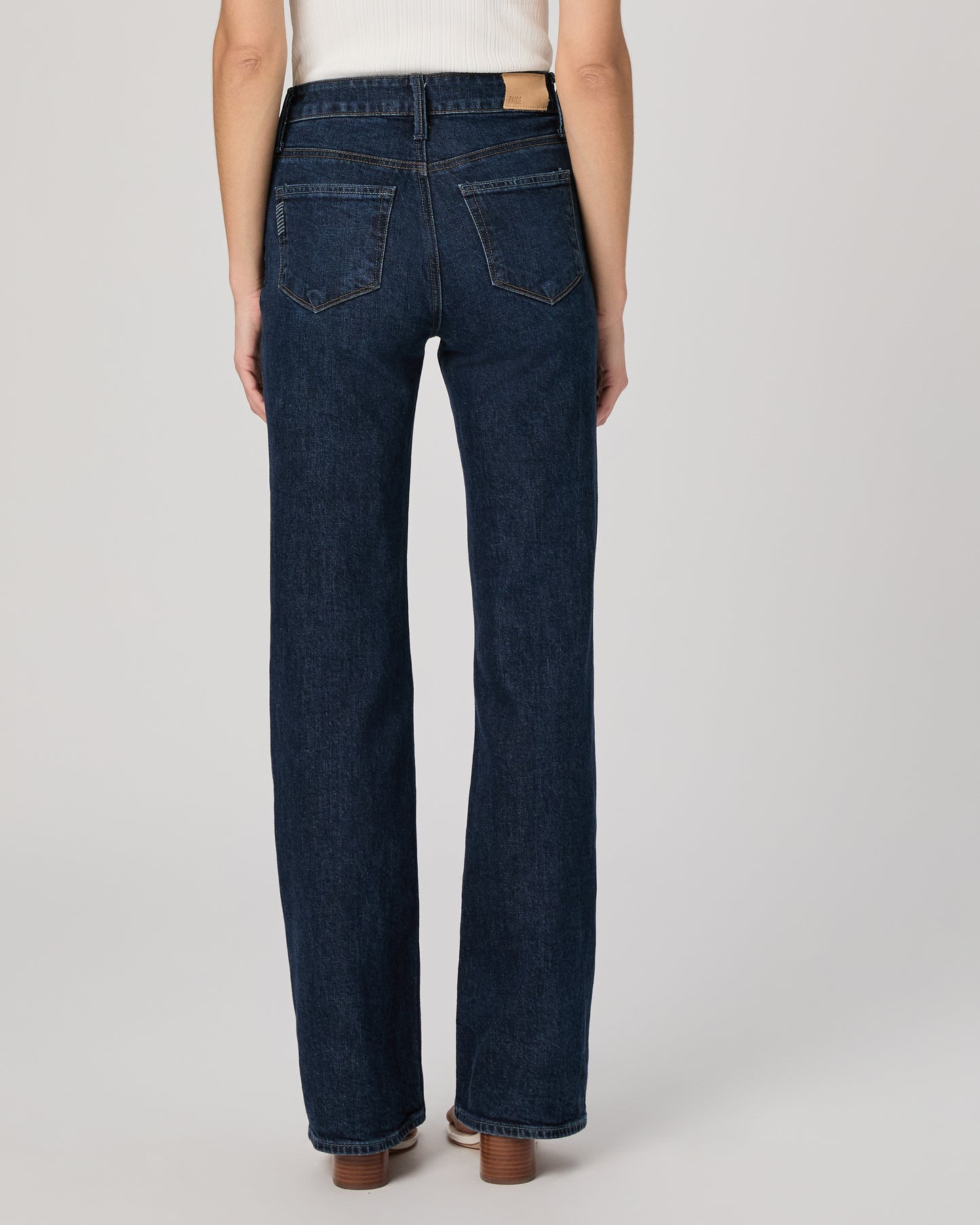 Person wearing dark blue jeans on a plain background