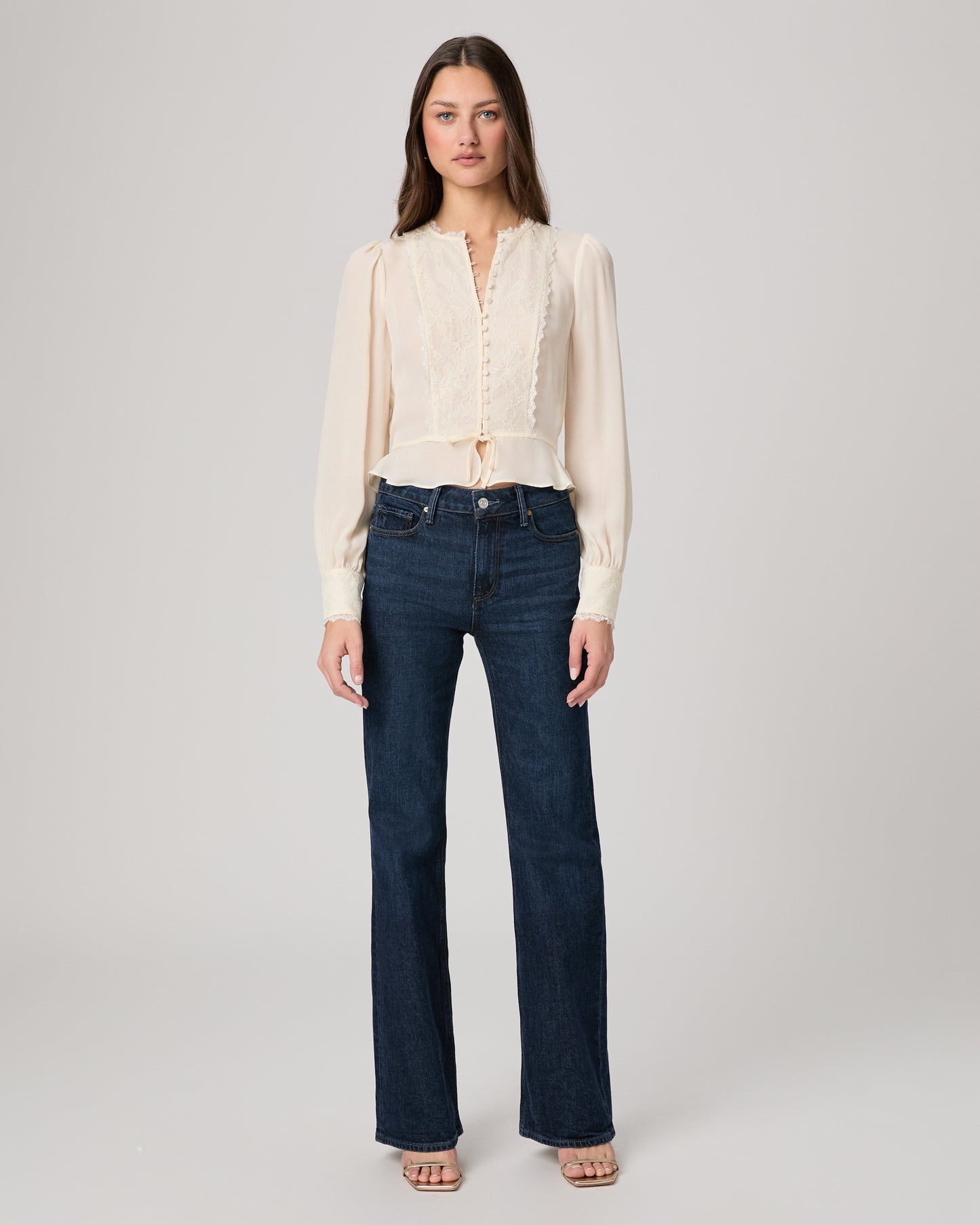 Woman wearing a white blouse and dark blue jeans on a plain background