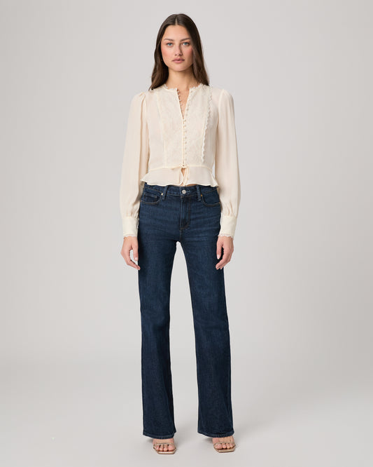 Woman wearing a white blouse and dark blue jeans on a plain background