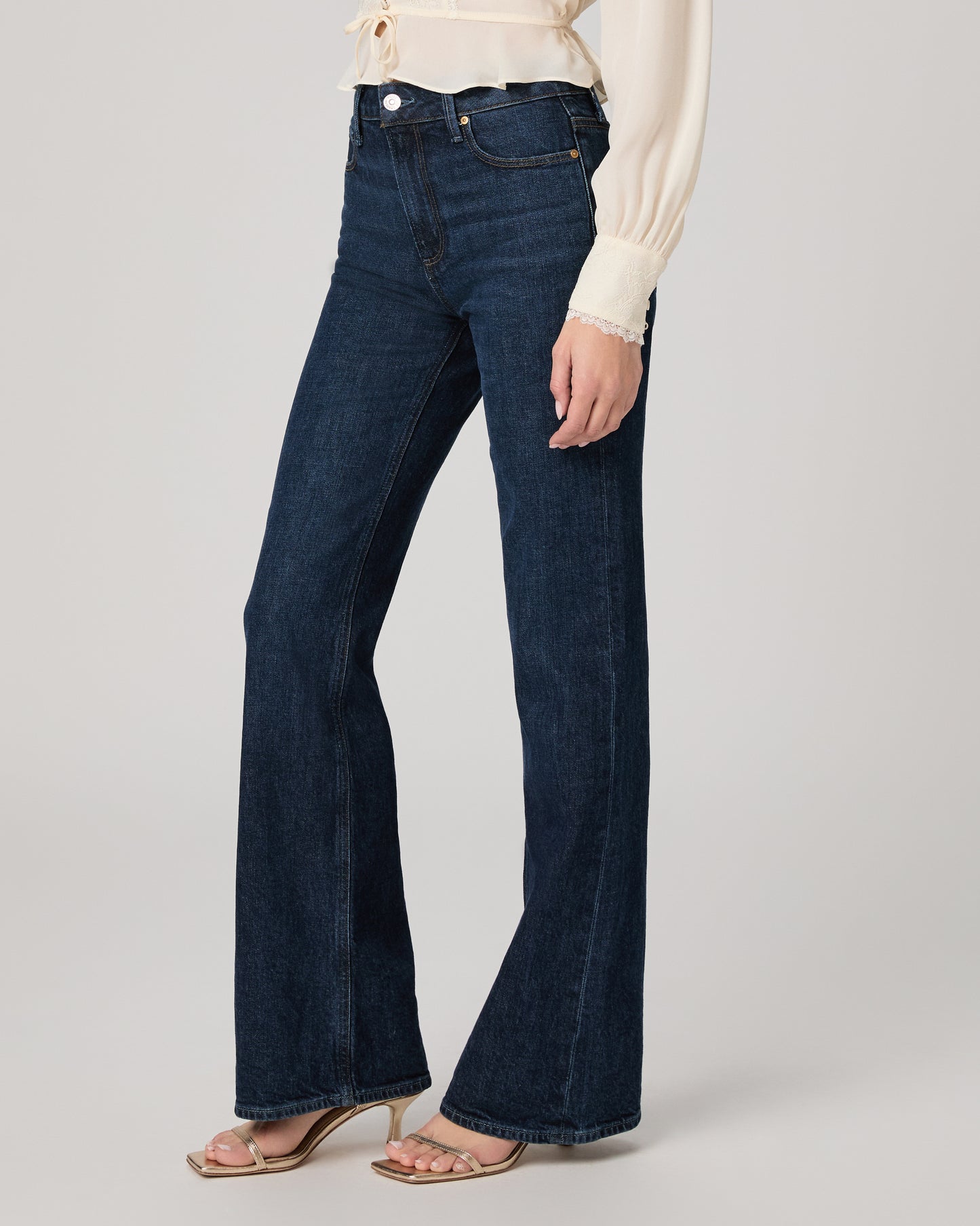Dark blue flared jeans worn by a person on a light gray background