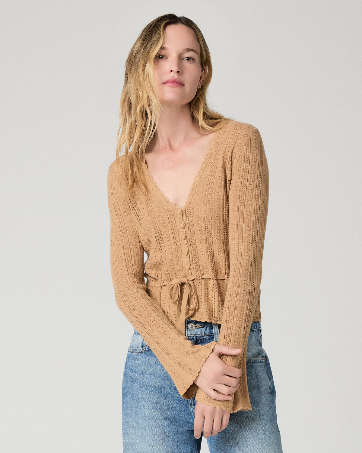 Women wearing a brown top paired with bllue jeans against a white background