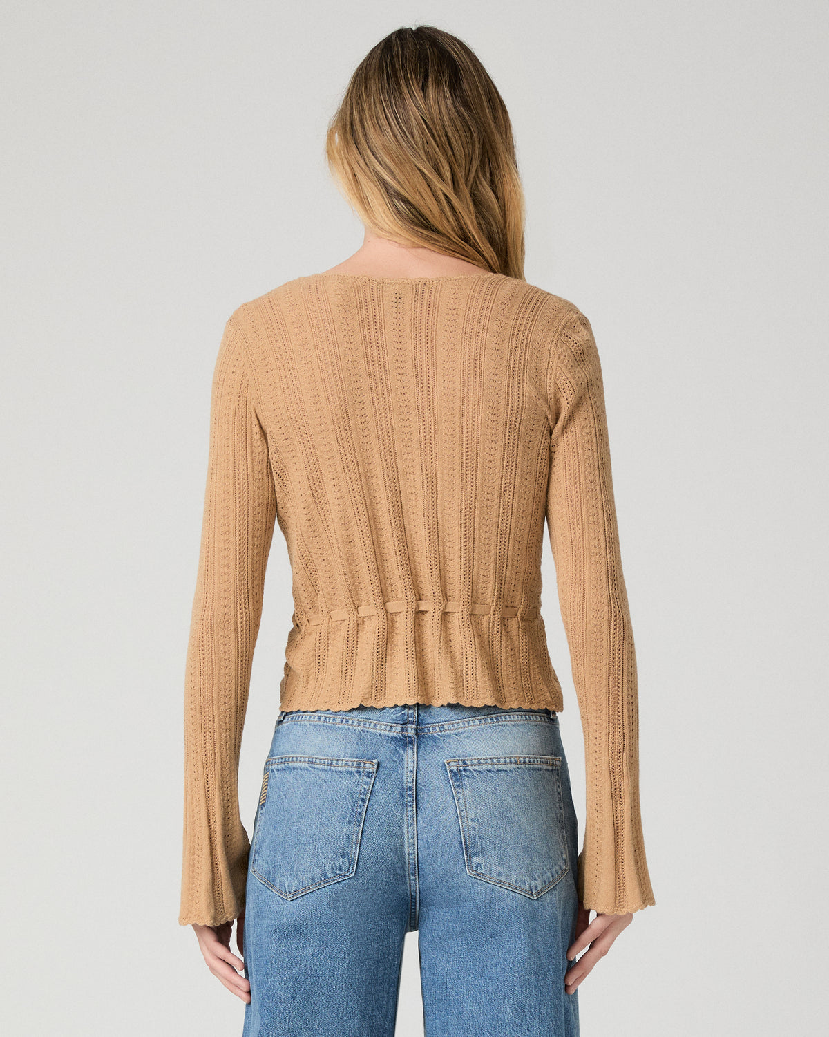 Women wearing a brown top paired with blue jeans against a white background