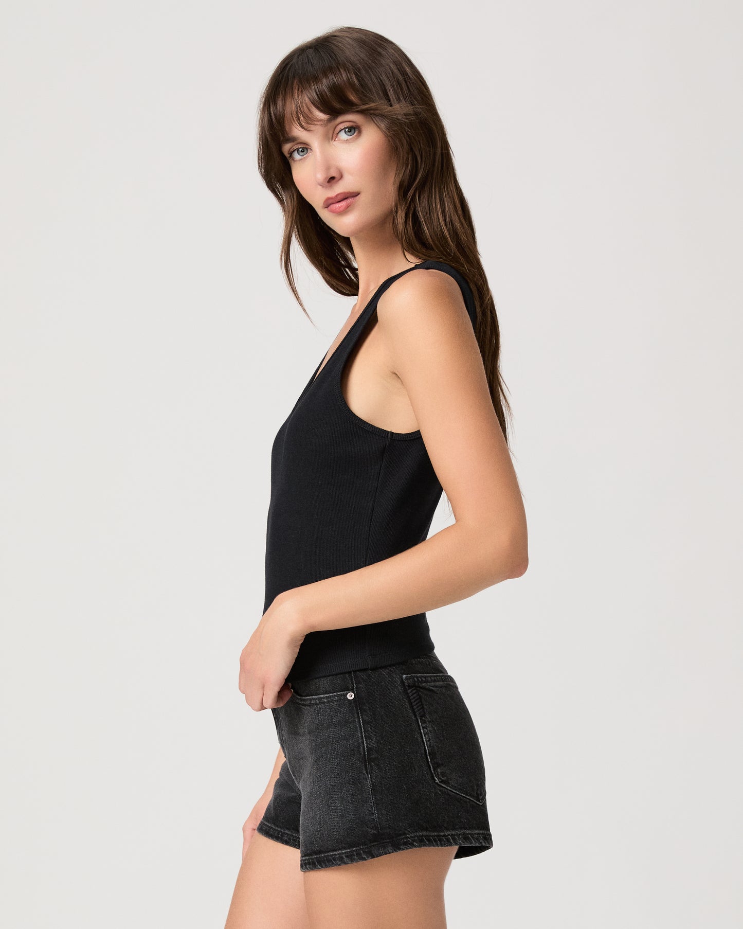Woman wearing a black tank top and dark denim shorts on a light gray background