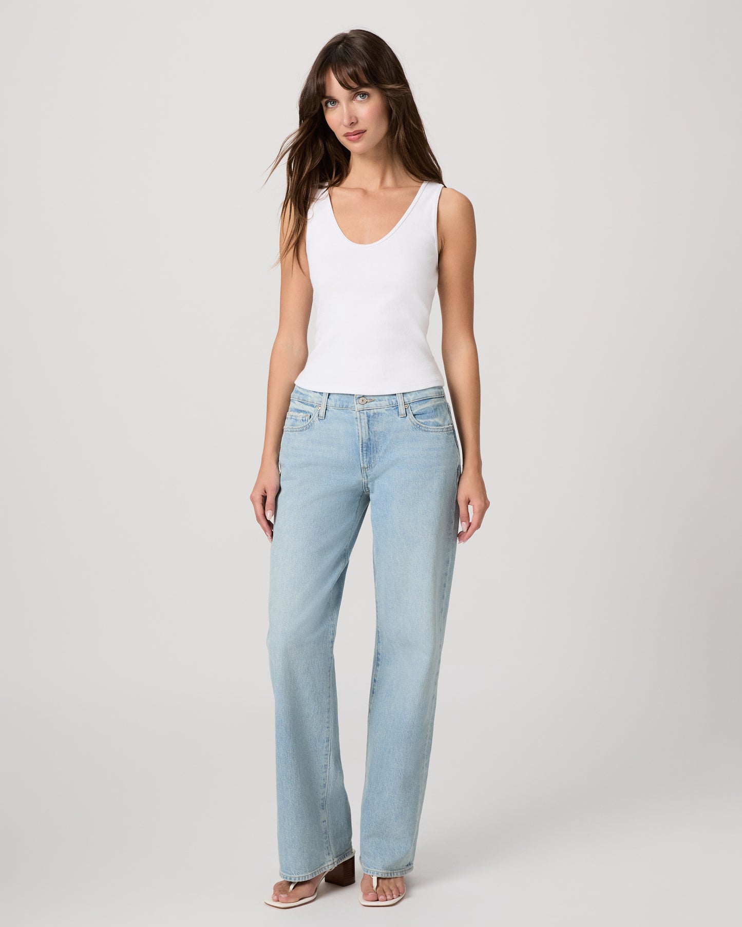 Woman wearing a white tank top and light blue jeans on a plain background