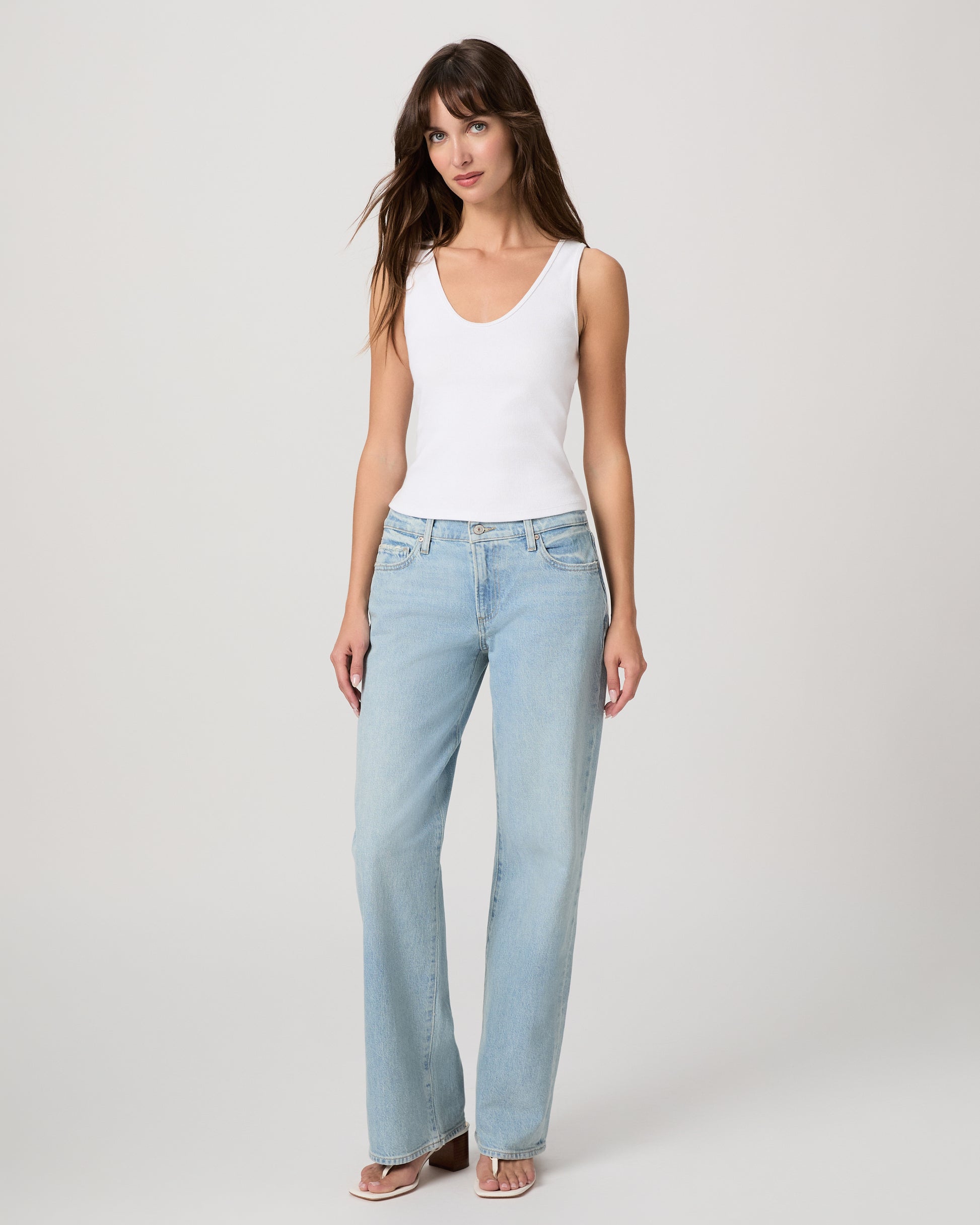 Woman wearing a white tank top and light blue jeans on a plain background