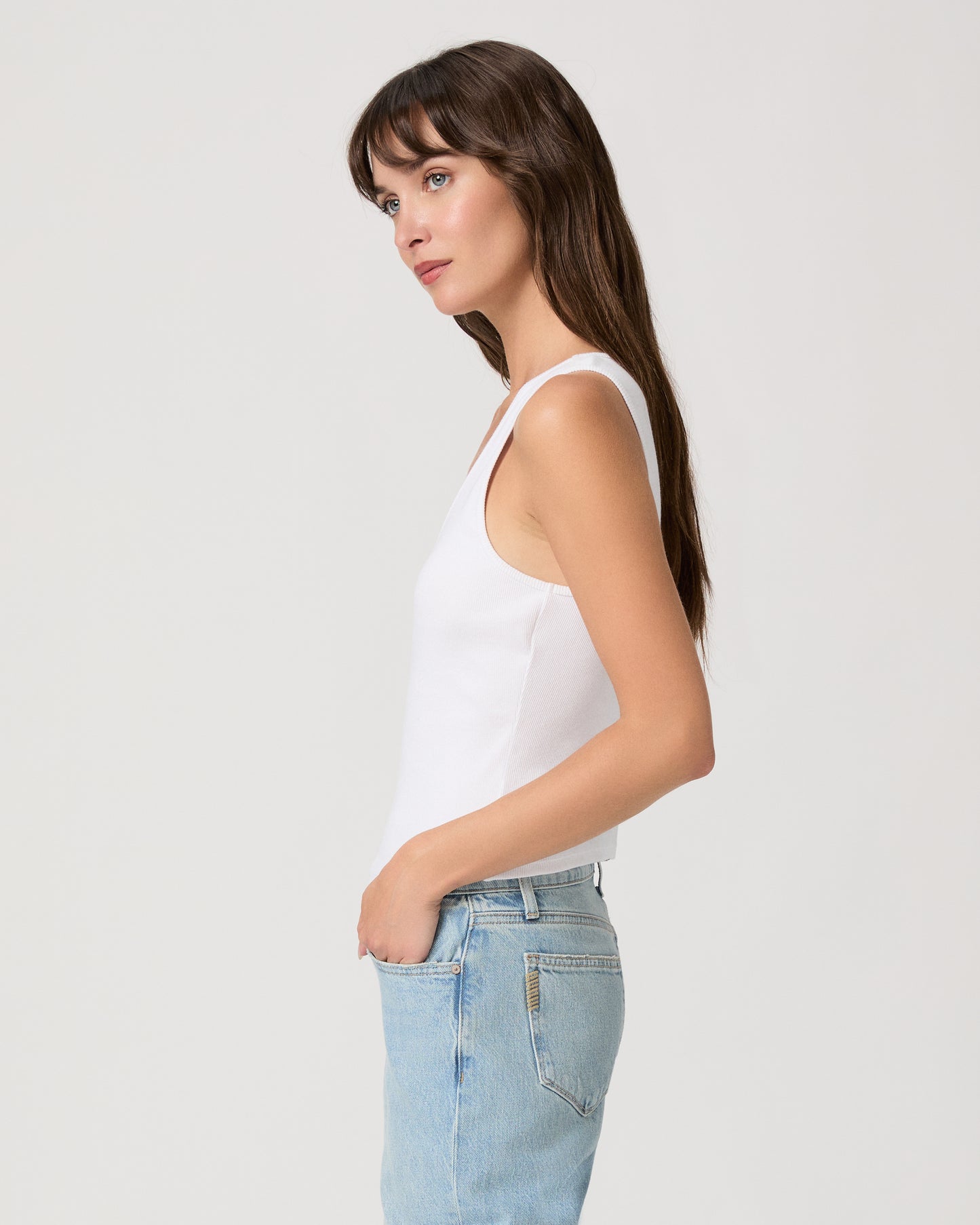 Woman wearing a white tank top and light blue jeans on a plain background