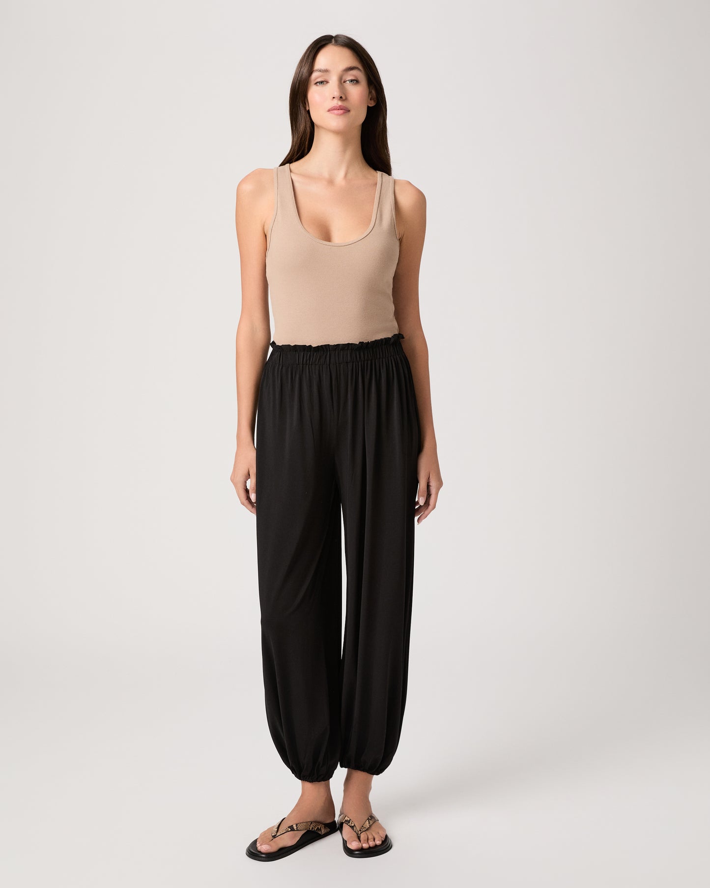 Model wearing a beige tank top paired with black pants and snake printed sandals