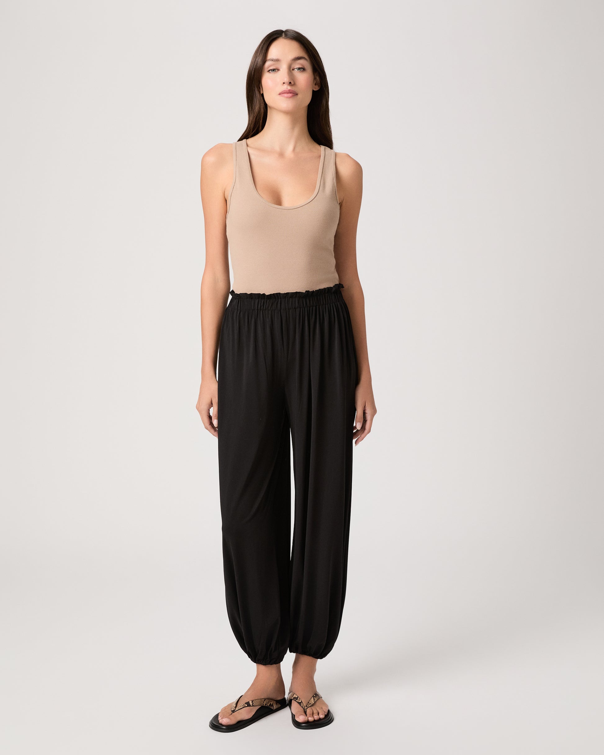 Model wearing a beige tank top paired with black pants and snake printed sandals