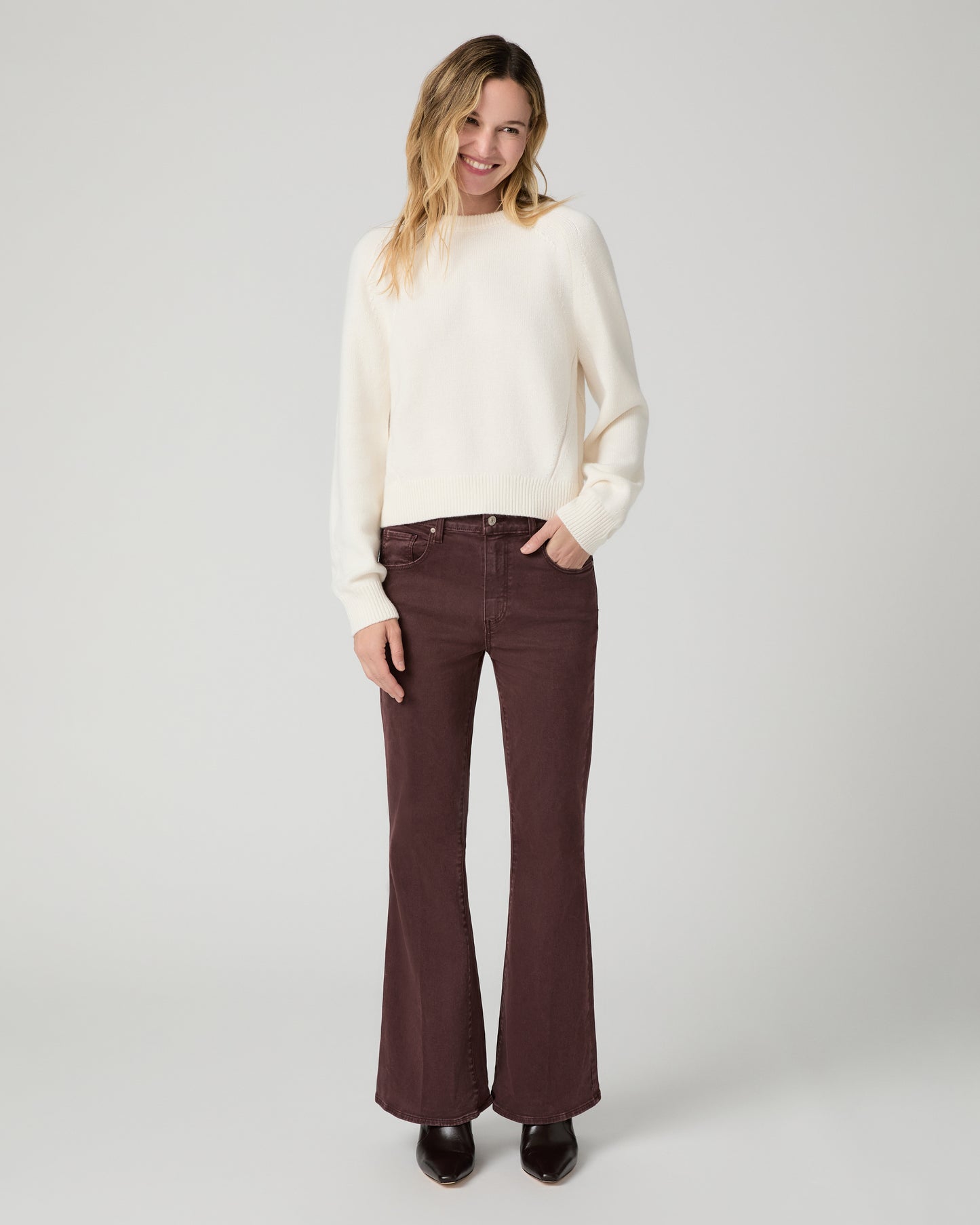 Women wearing a white long sleeve sweater paired with burgundy jeans and brown boots against a white background