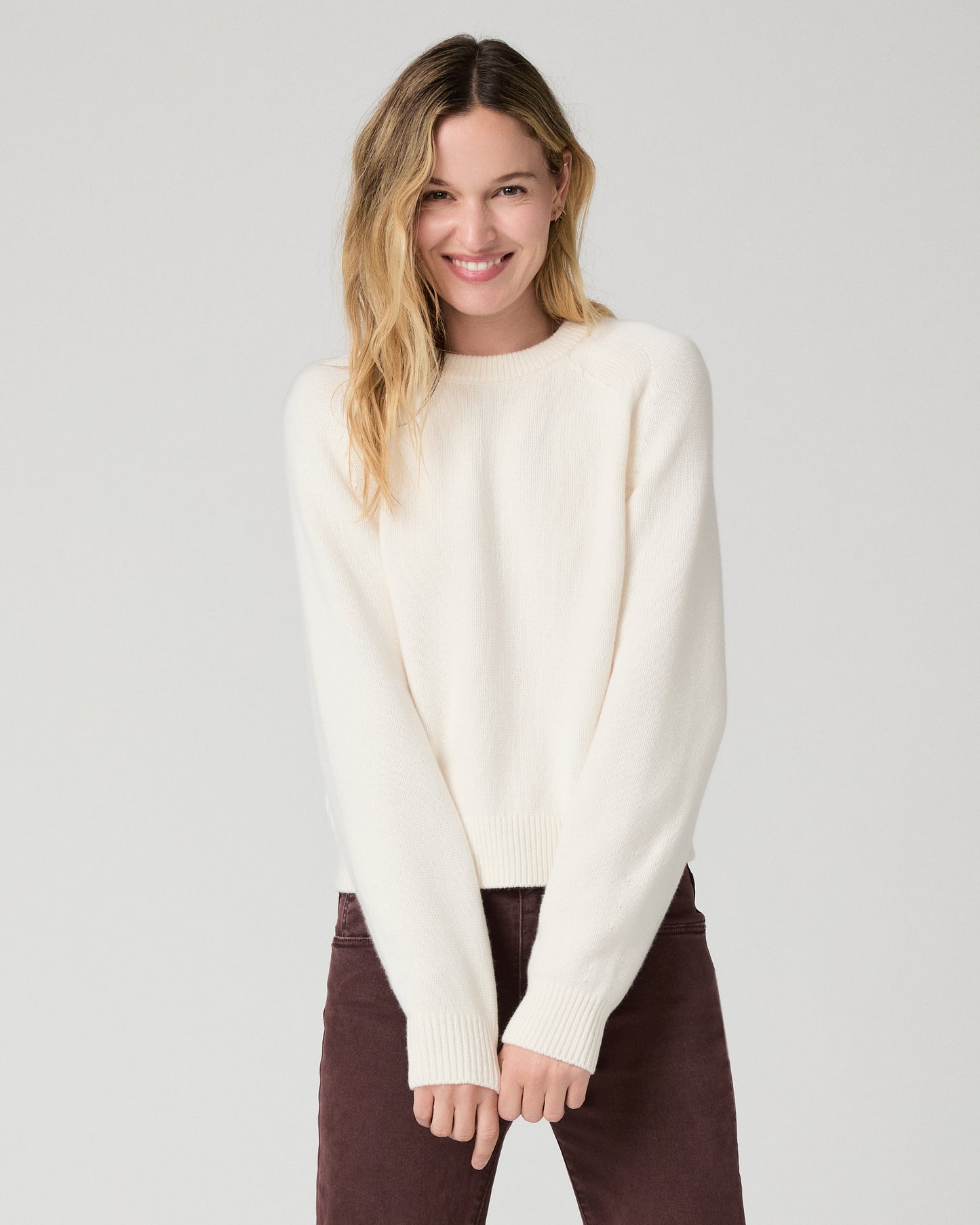 Women wearing a white long sleeve sweater paired with burgundy jeans against a white background