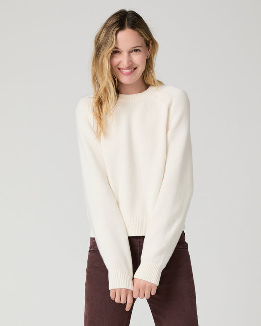 Women wearing a white long sleeve sweater paired with burgundy jeans against a white background