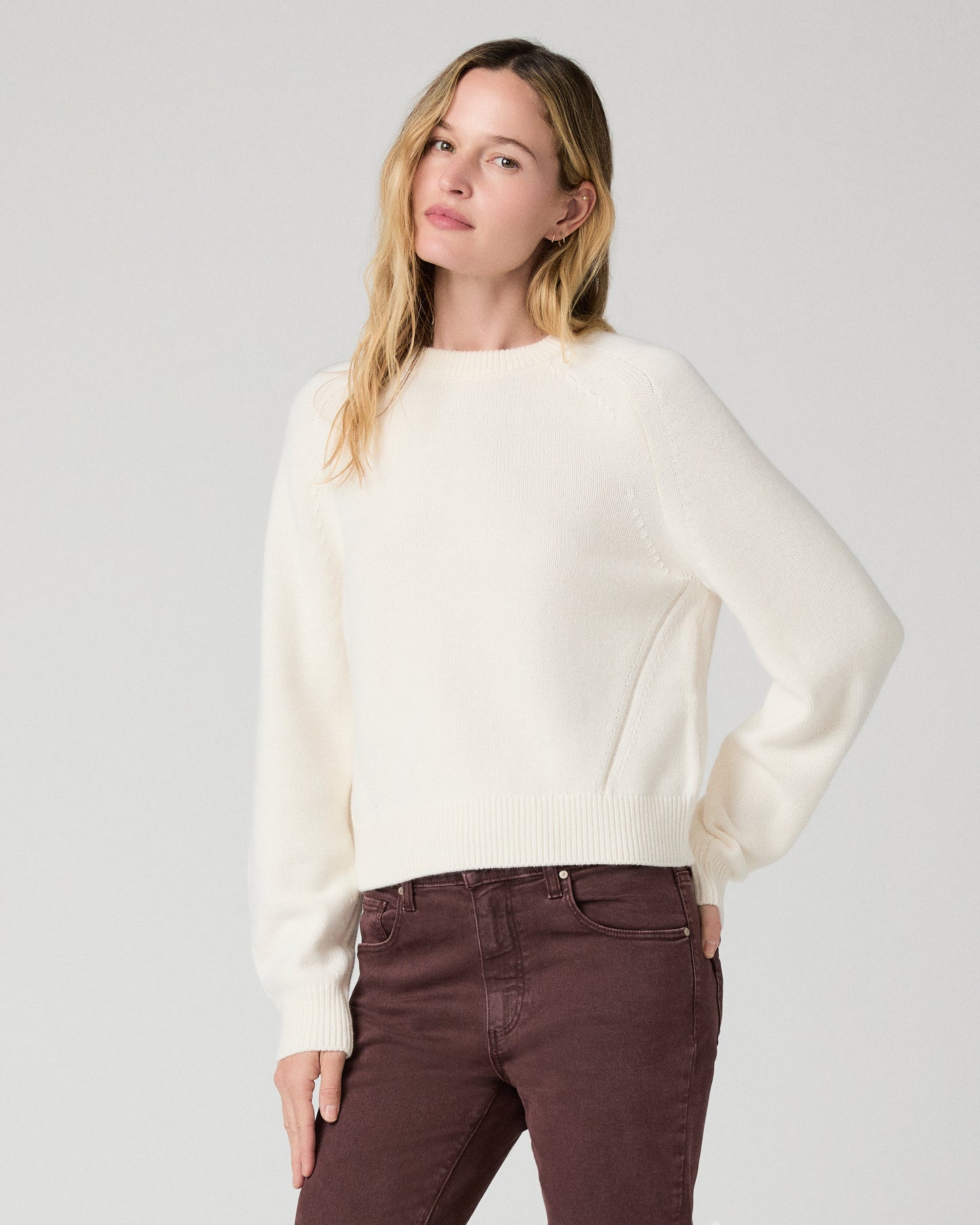 Women wearing a white long sleeve sweater paired with burgundy jean against a white background