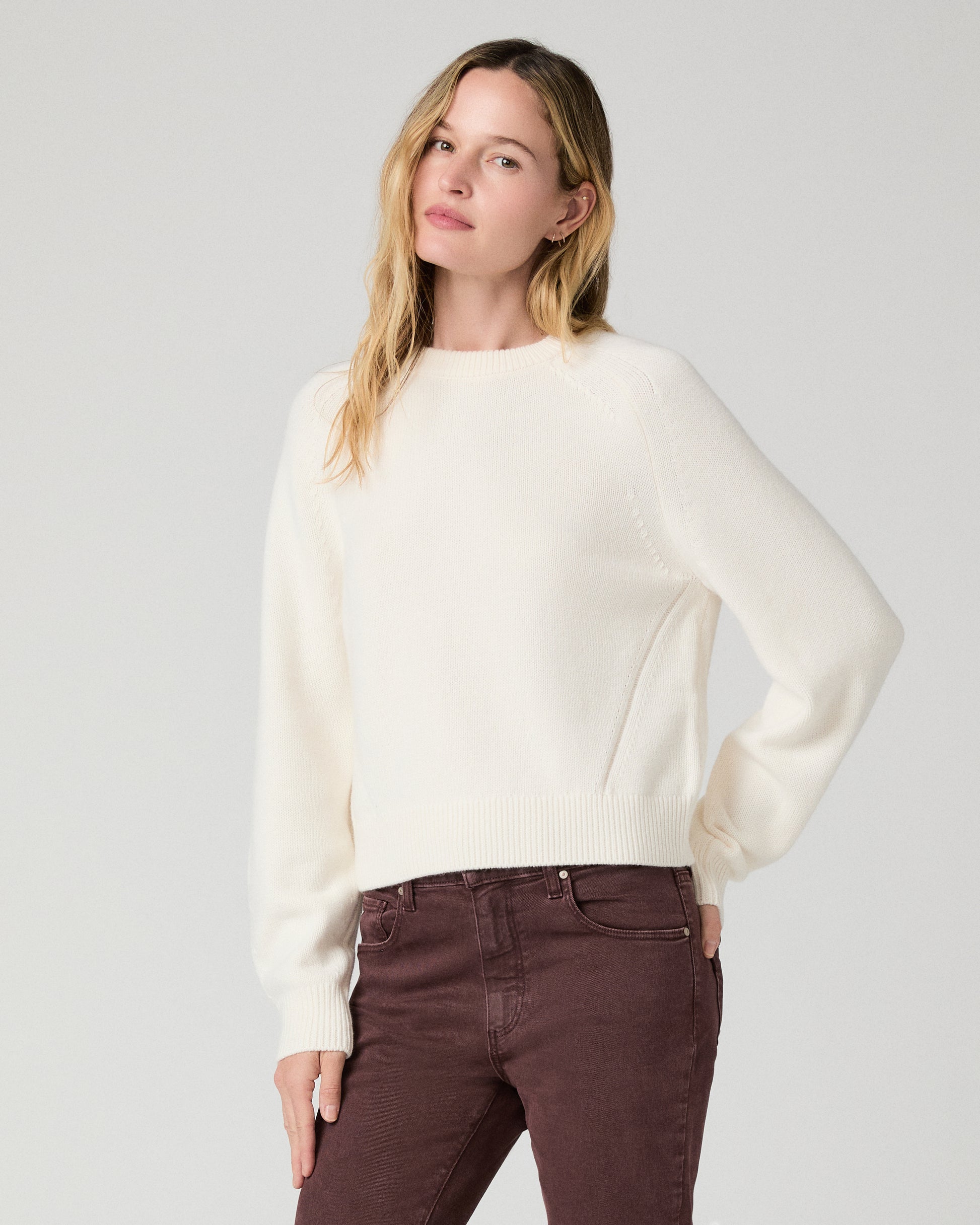 Women wearing a white long sleeve sweater paired with burgundy jean against a white background