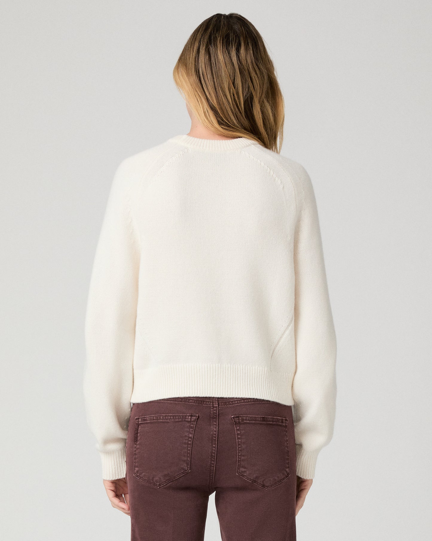 Women wearing a white long sleeve sweater paired with burgundy jean against a white background