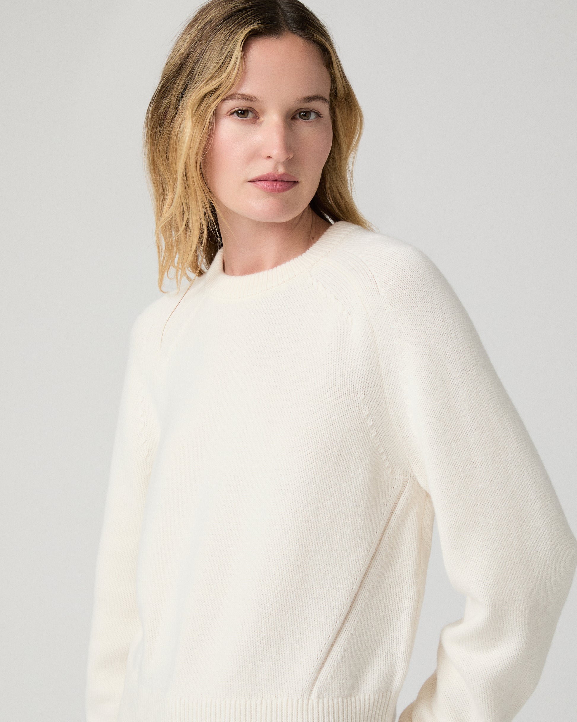 Women wearing a white long sleeve sweater paired with burgundy jean against a white background
