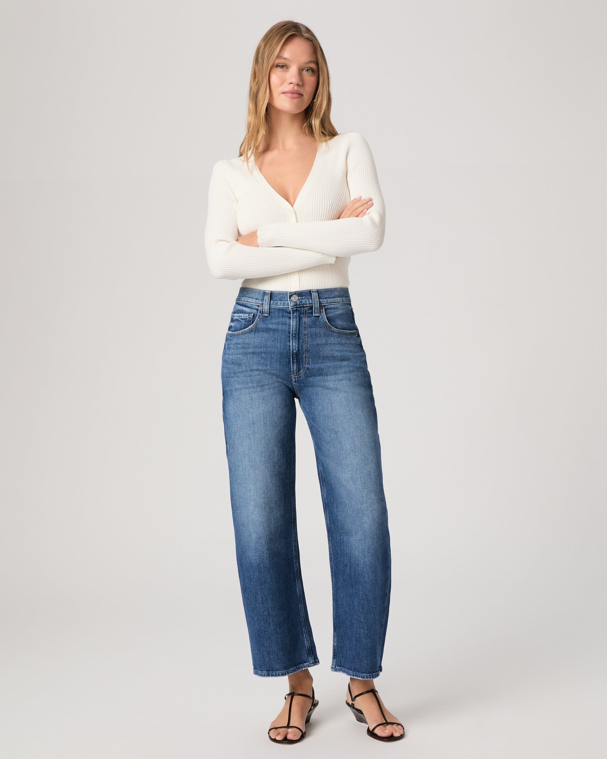 Model wearing a white long sleeve op paired with medium wash jeans and brown sandals against a white background. 