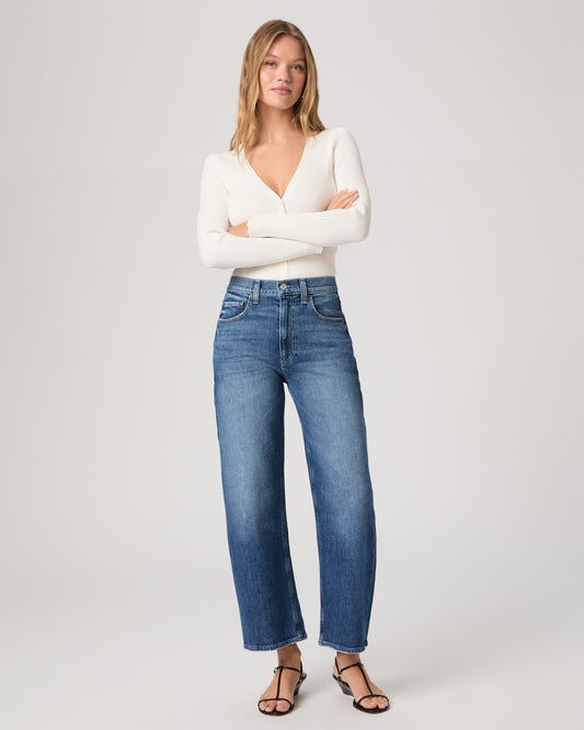 Model wearing a white long sleeve op paired with medium wash jeans and brown sandals against a white background. 