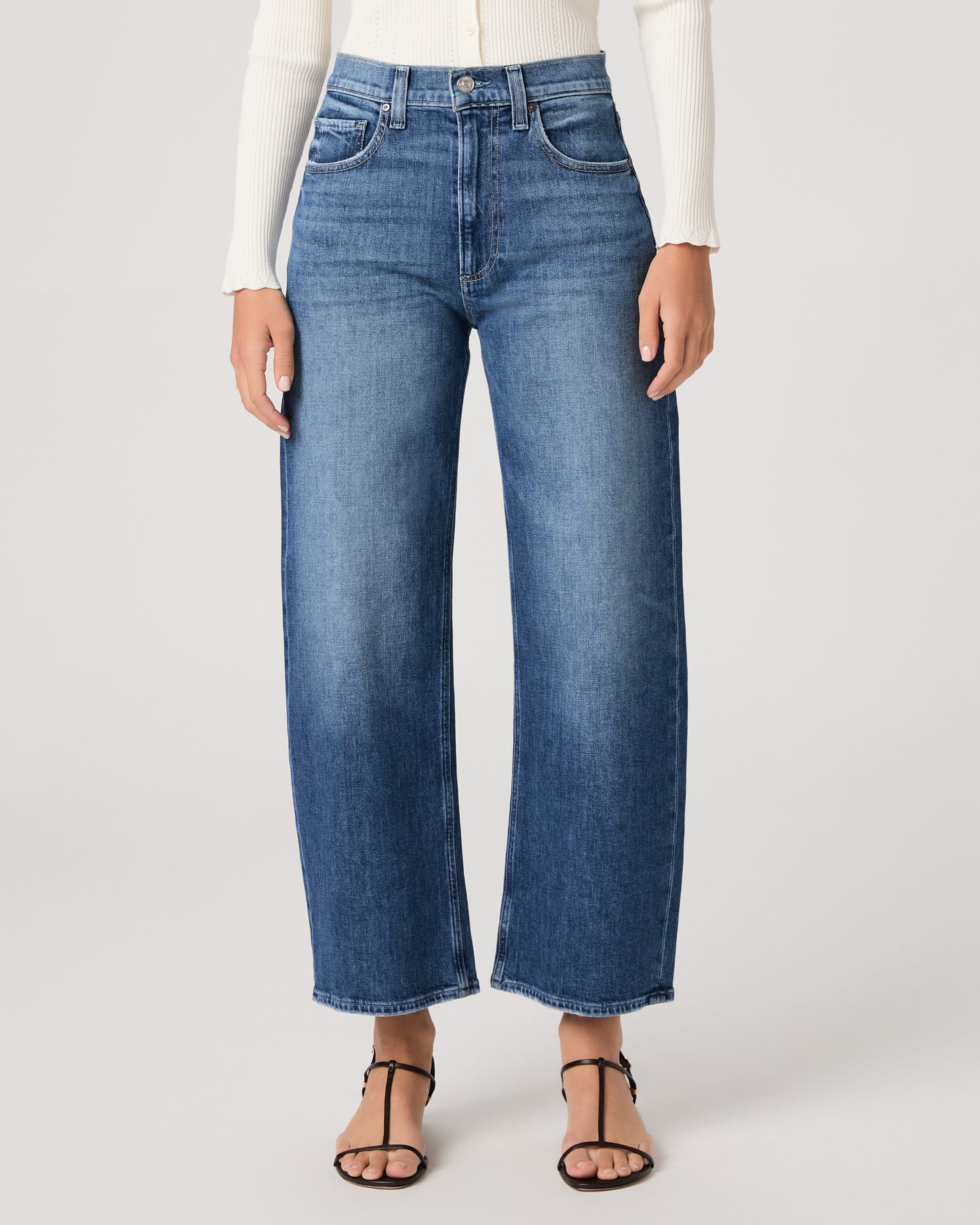 Model wearing a white long sleeve op paired with medium wash jeans and brown sandals against a white background. 