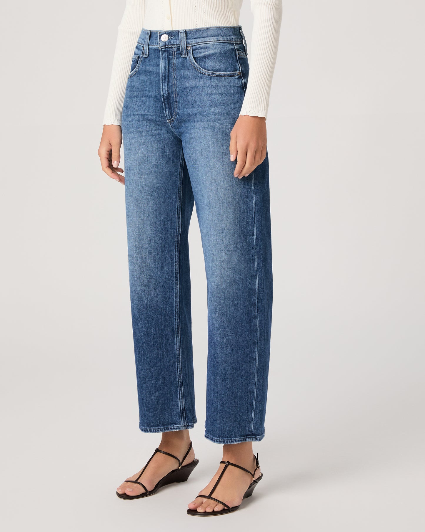 Model wearing a white long sleeve op paired with medium wash jeans and brown sandals against a white background. 
