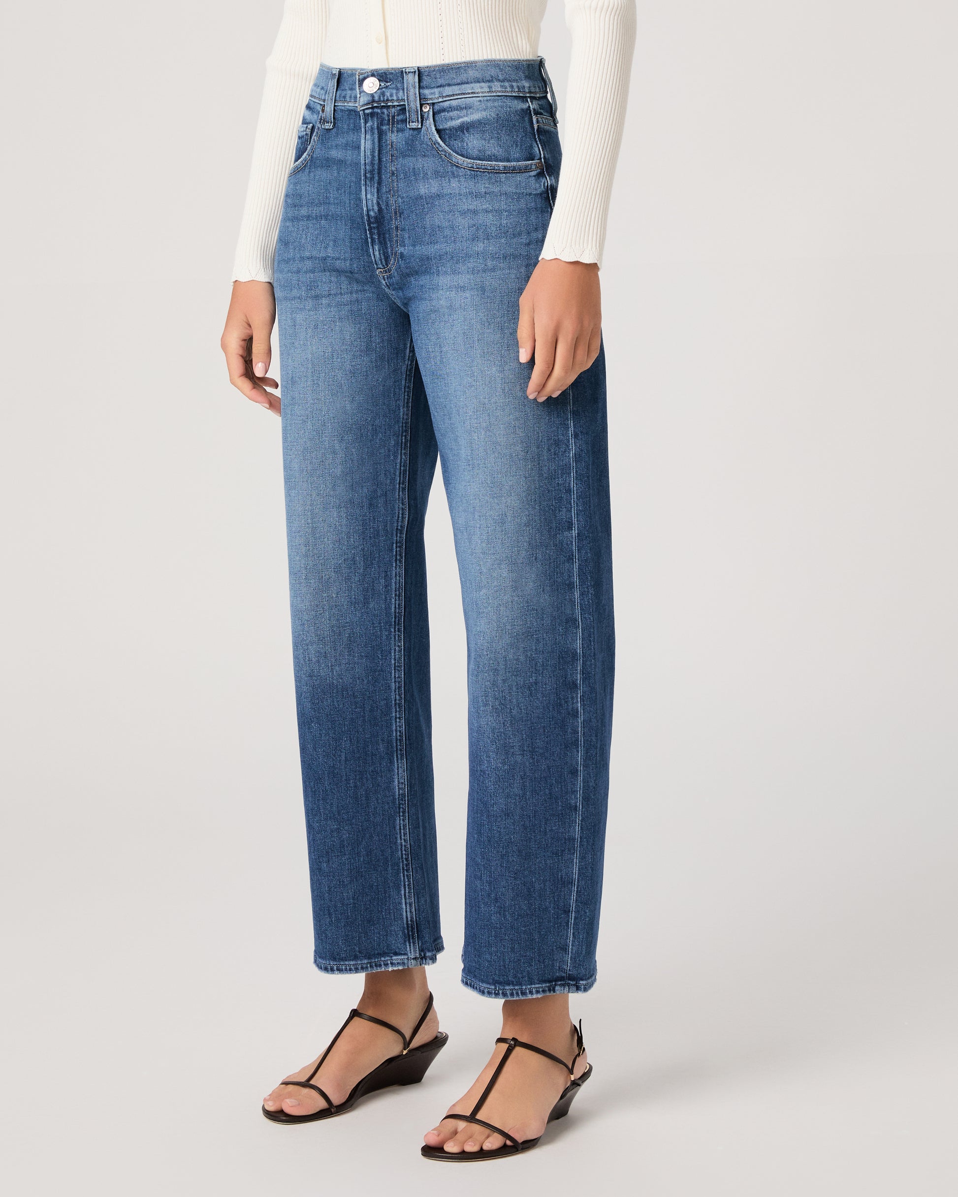 Model wearing a white long sleeve op paired with medium wash jeans and brown sandals against a white background. 