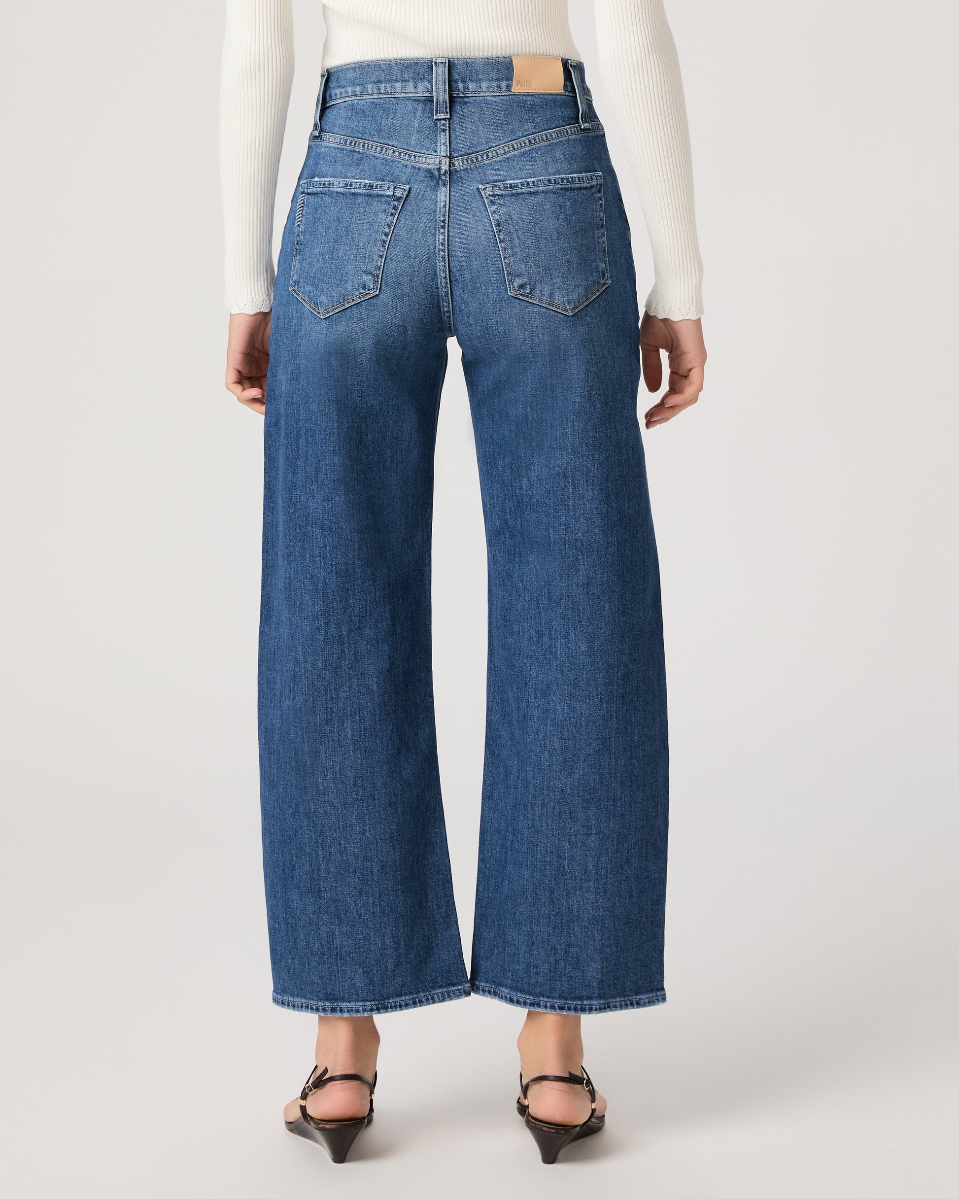 Model wearing a white long sleeve op paired with medium wash jeans and brown sandals against a white background. 
