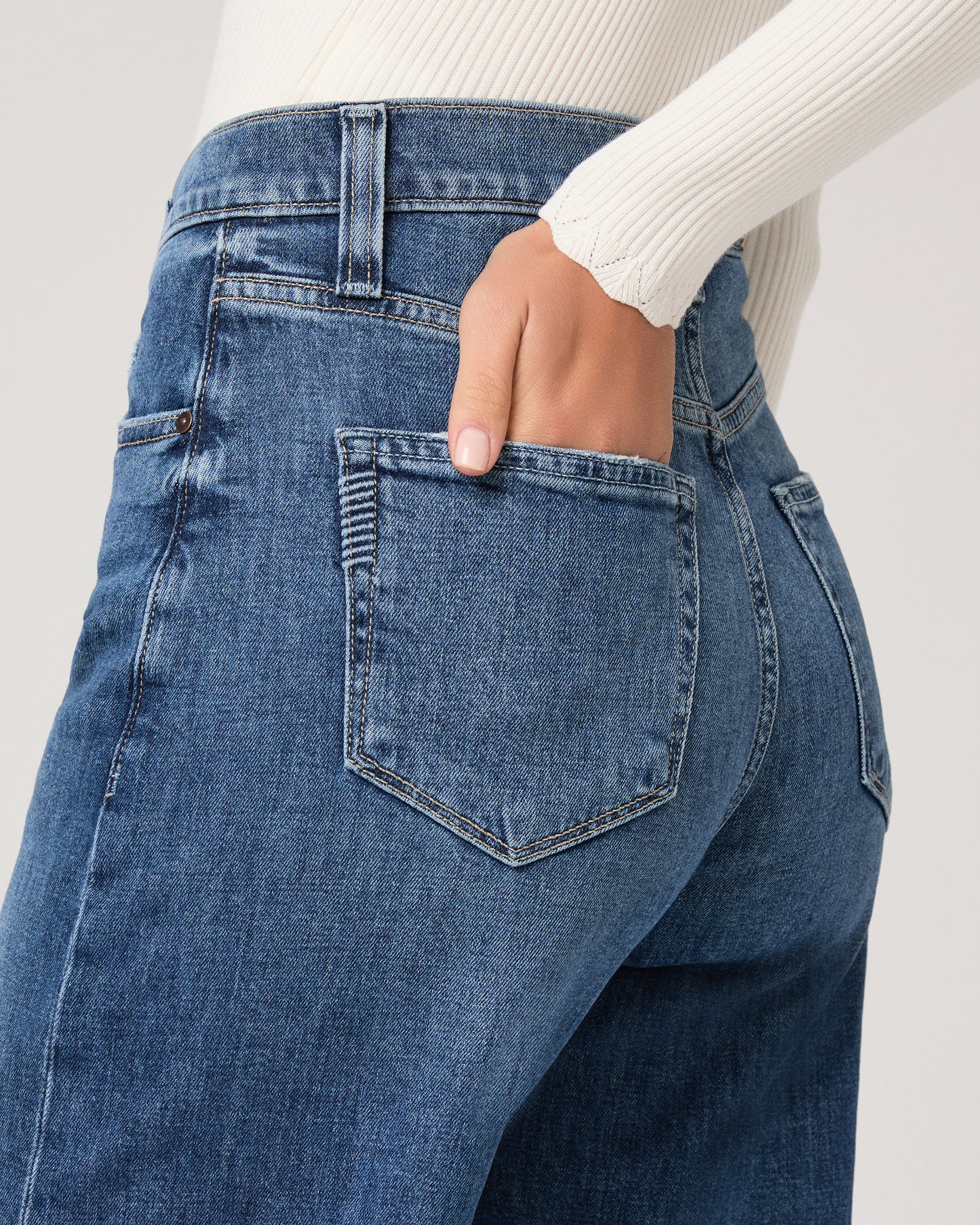 Model wearing a white long sleeve op paired with medium wash jeans and brown sandals against a white background. 