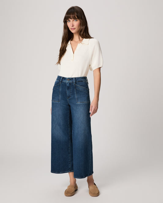 Woman wearing a white blouse and blue jeans, light brown flats on a plain background