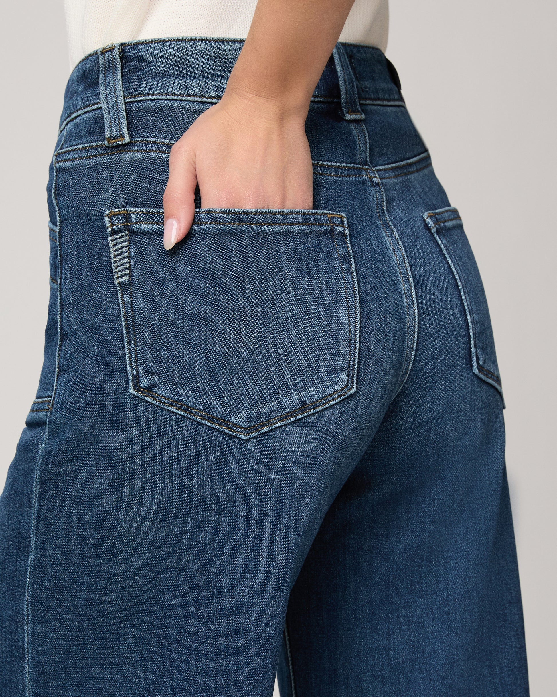 Woman wearing a white blouse and blue jeans on a plain background