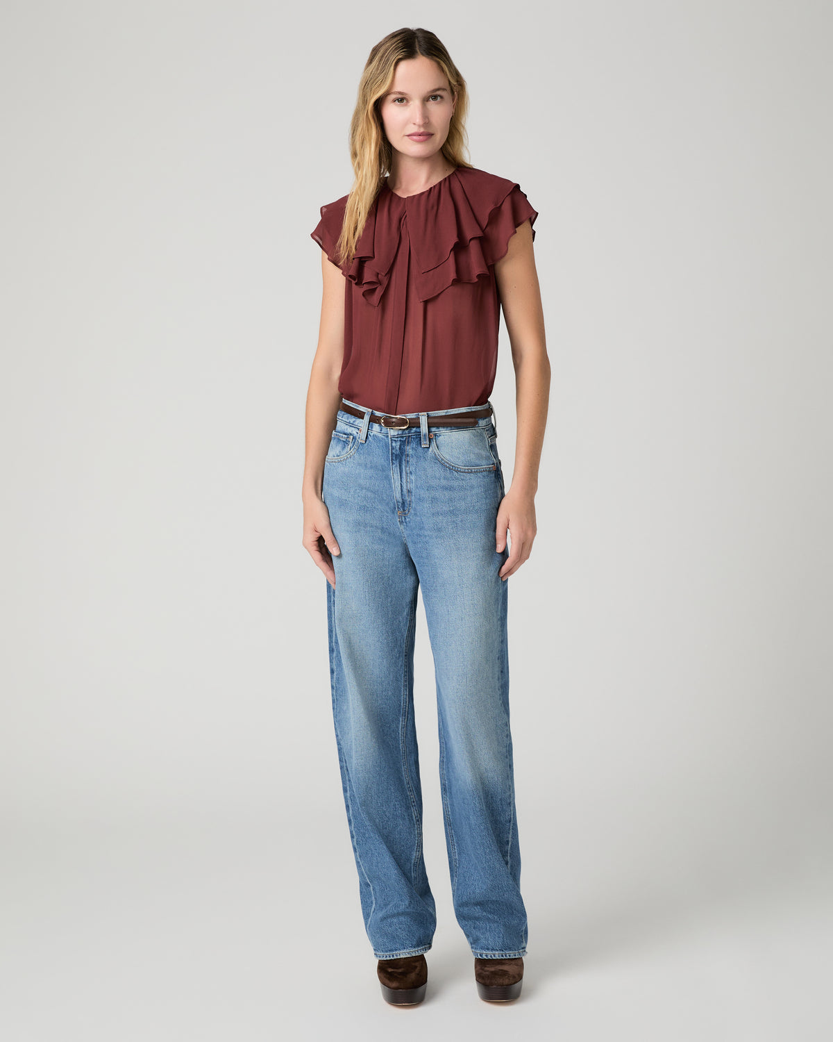Women wearing red blouse and blue jeans  paired with brown boots and a brown belt against a white background