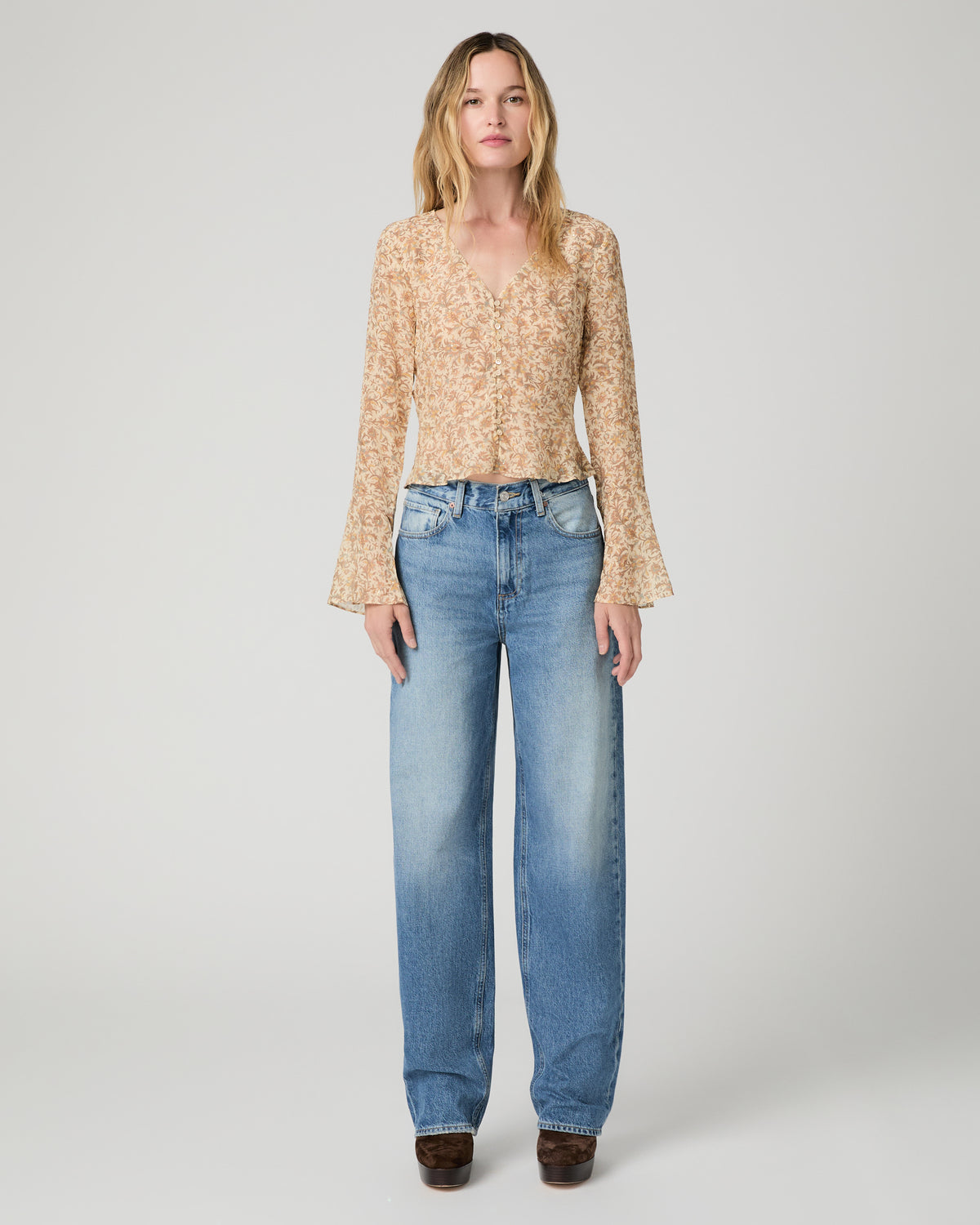 Women wearing a flower printed brown blouse and blue jeans paired with brown boots against a white background