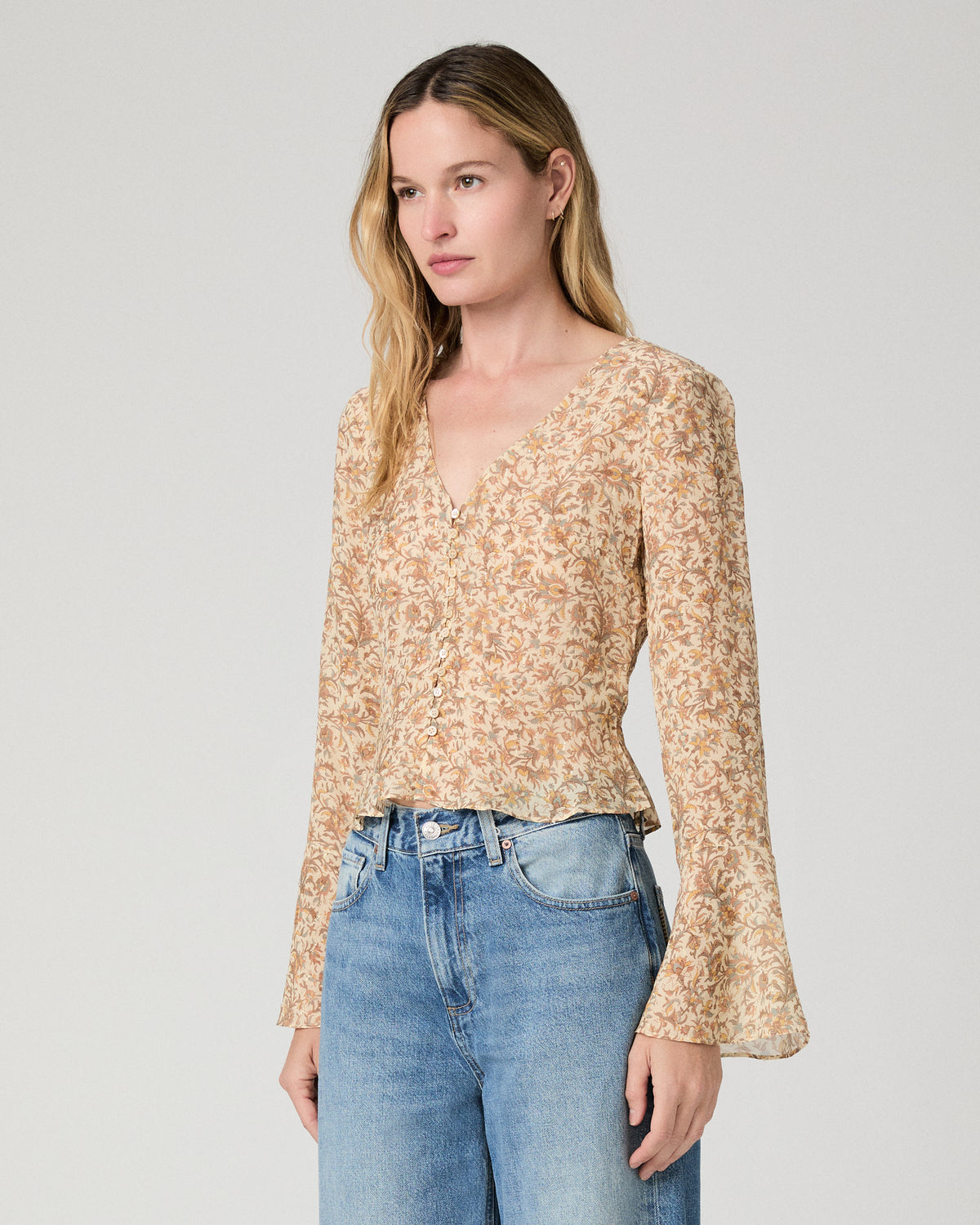 Women wearing a flower printed brown blouse and blue jeans against a white background
