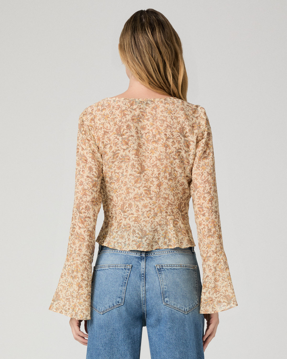 Women wearing a flower printed brown blouse and blue jeans against a white background