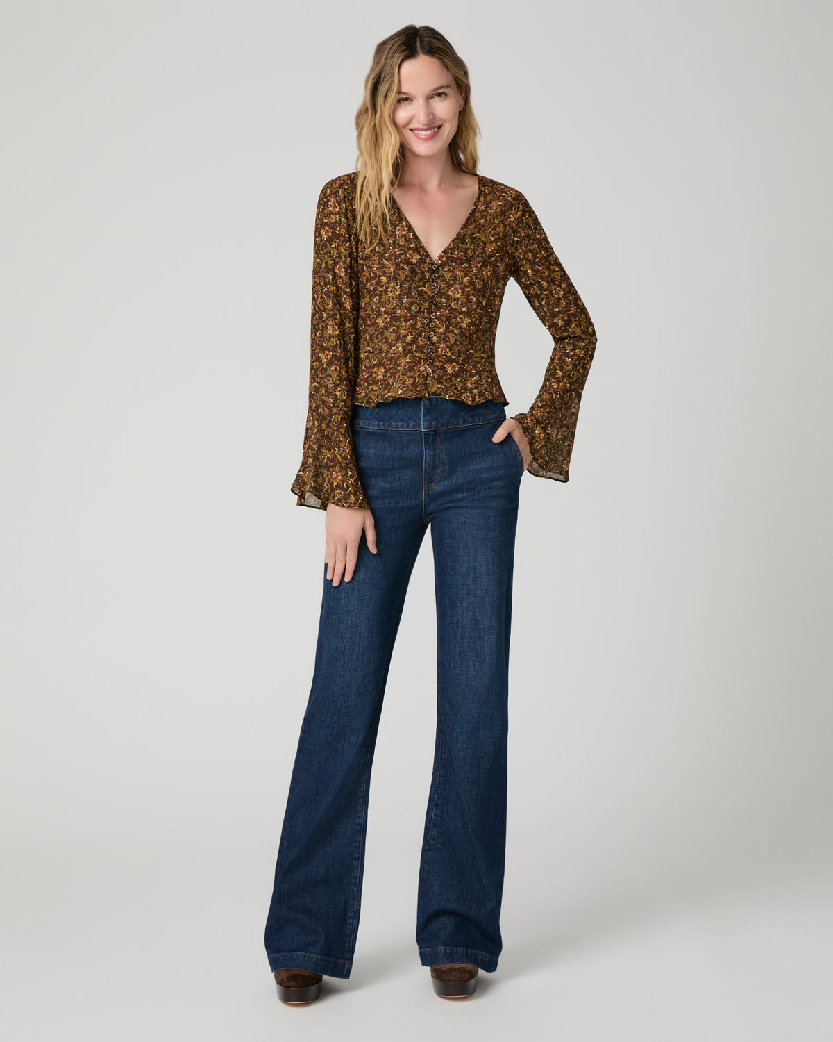 Women wearing a flower print blouse paired with blue jeans and brown boots against a white background