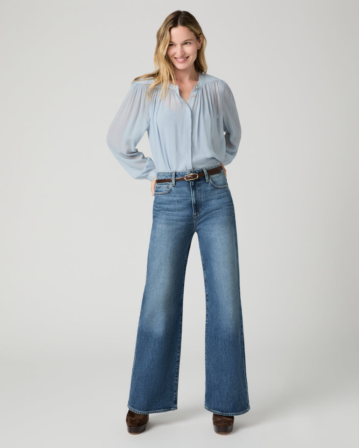Women wearing a light blue blouse and blue jeans paired with brown boots and a brown belt against a white background