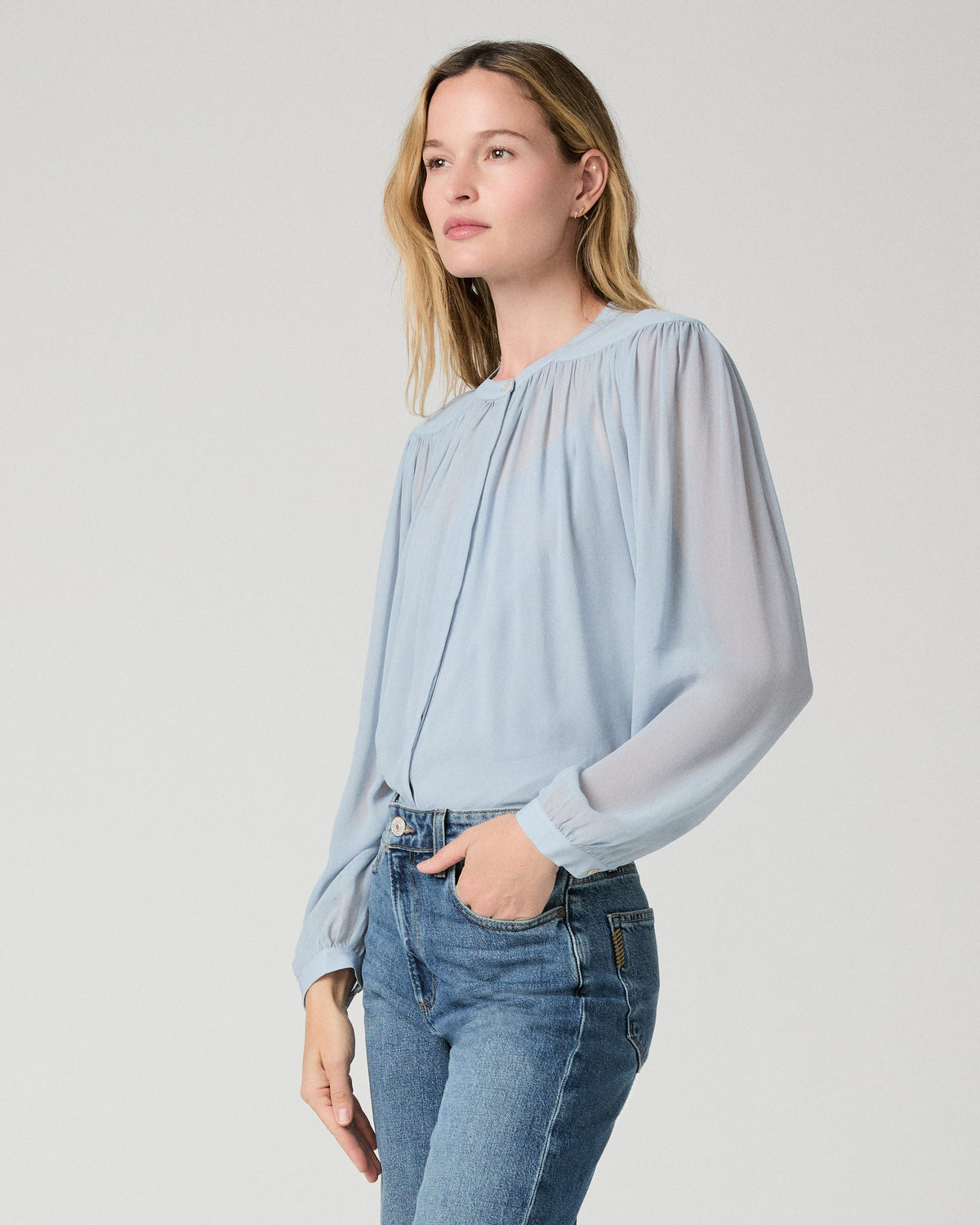 Women wearing a light blue blouse and blue jeans against a white background