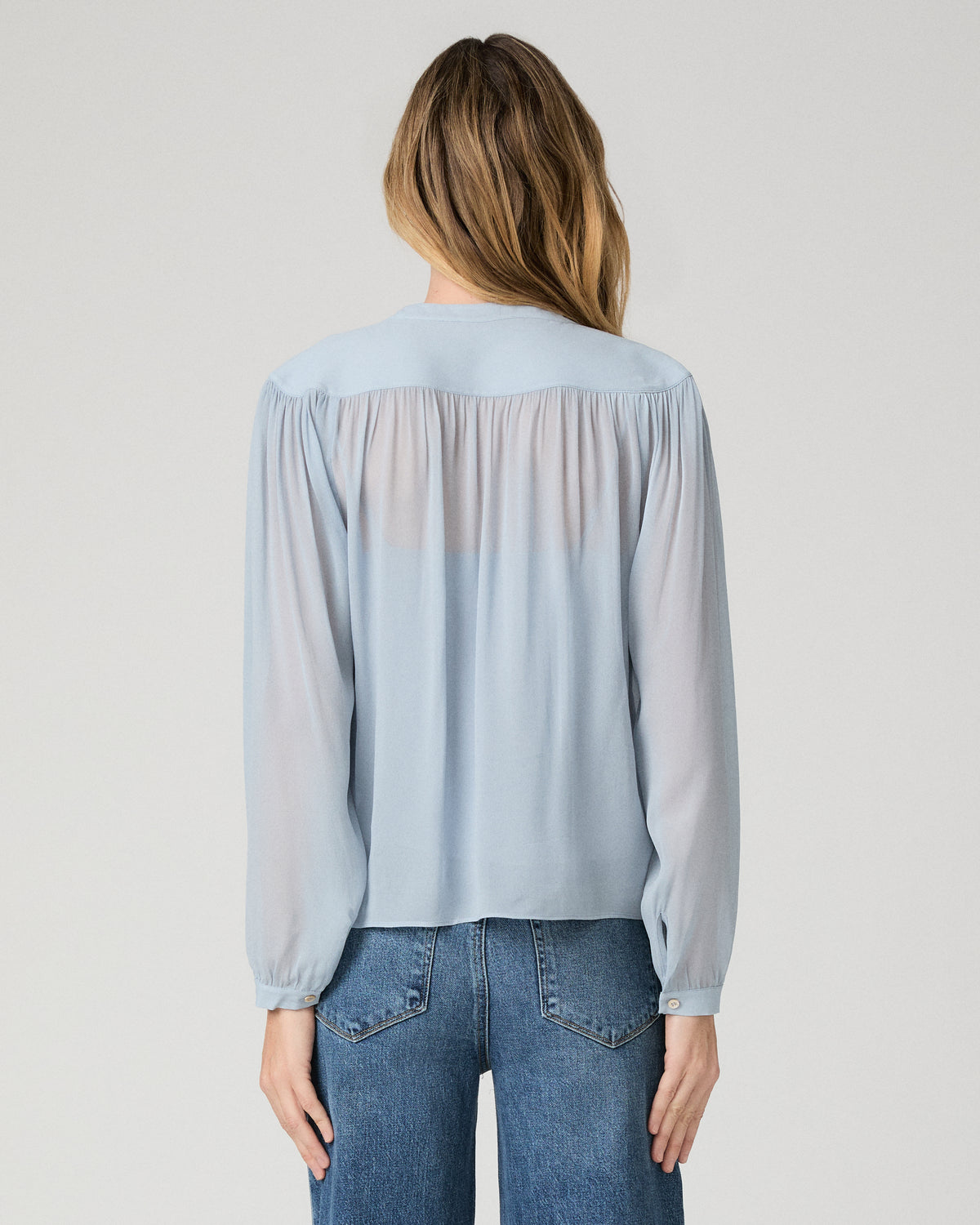Women wearing a light blue blouse and blue jeans against a white background