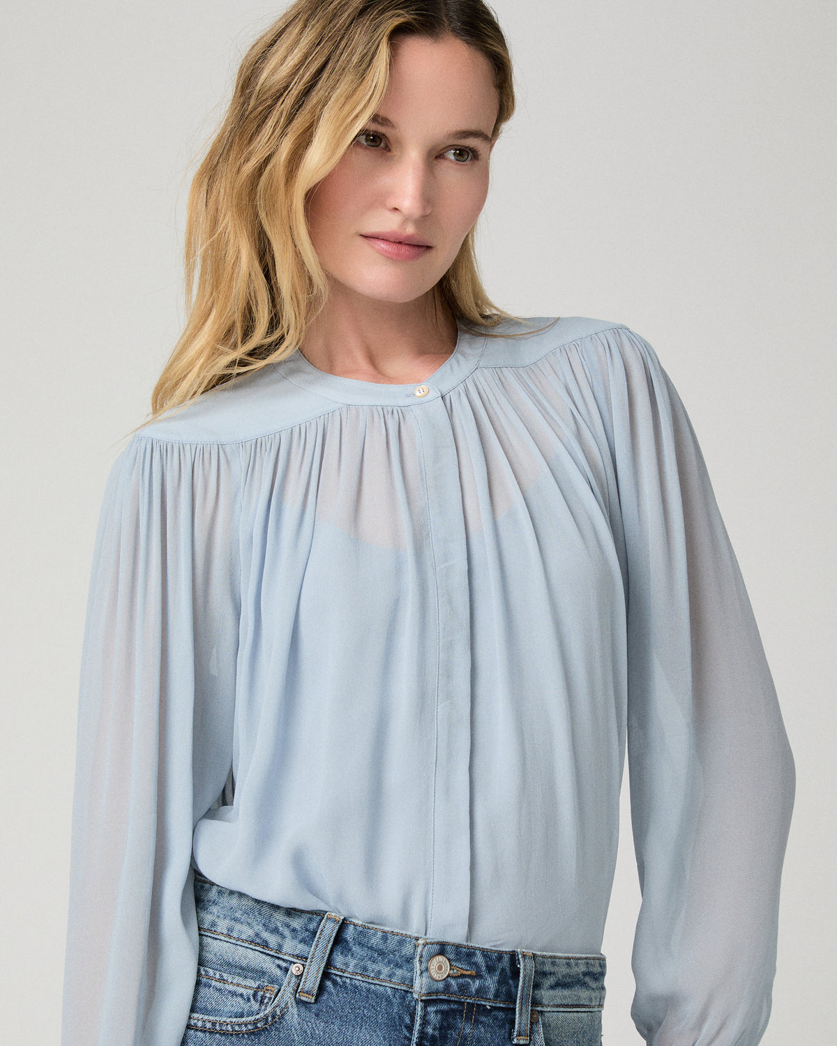 Women wearing a light blue blouse and blue jeans against a white background