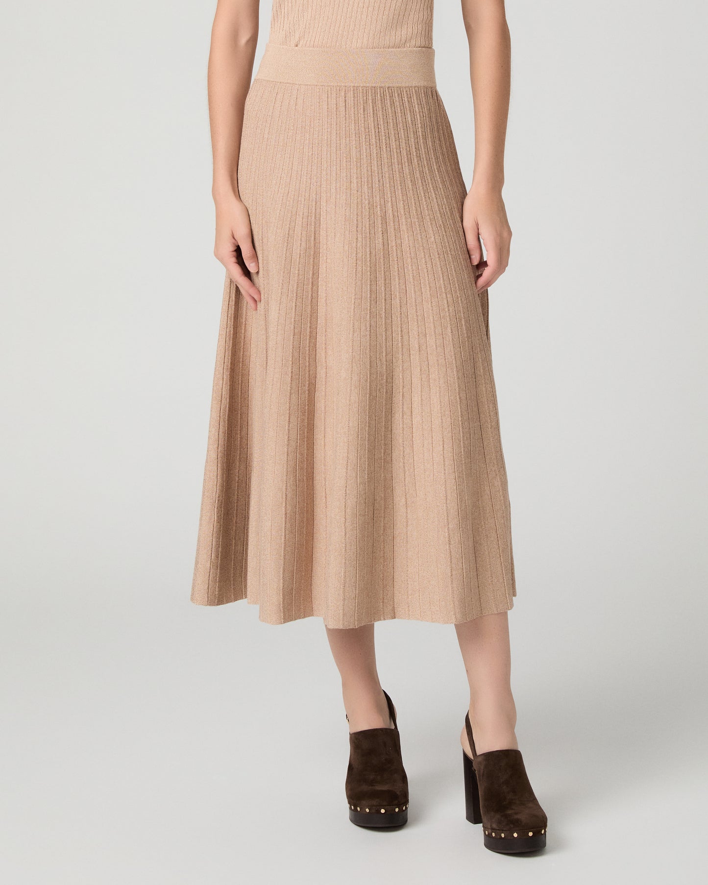 Women wearing a tan top and matching skirt paired with brown heels against a white background