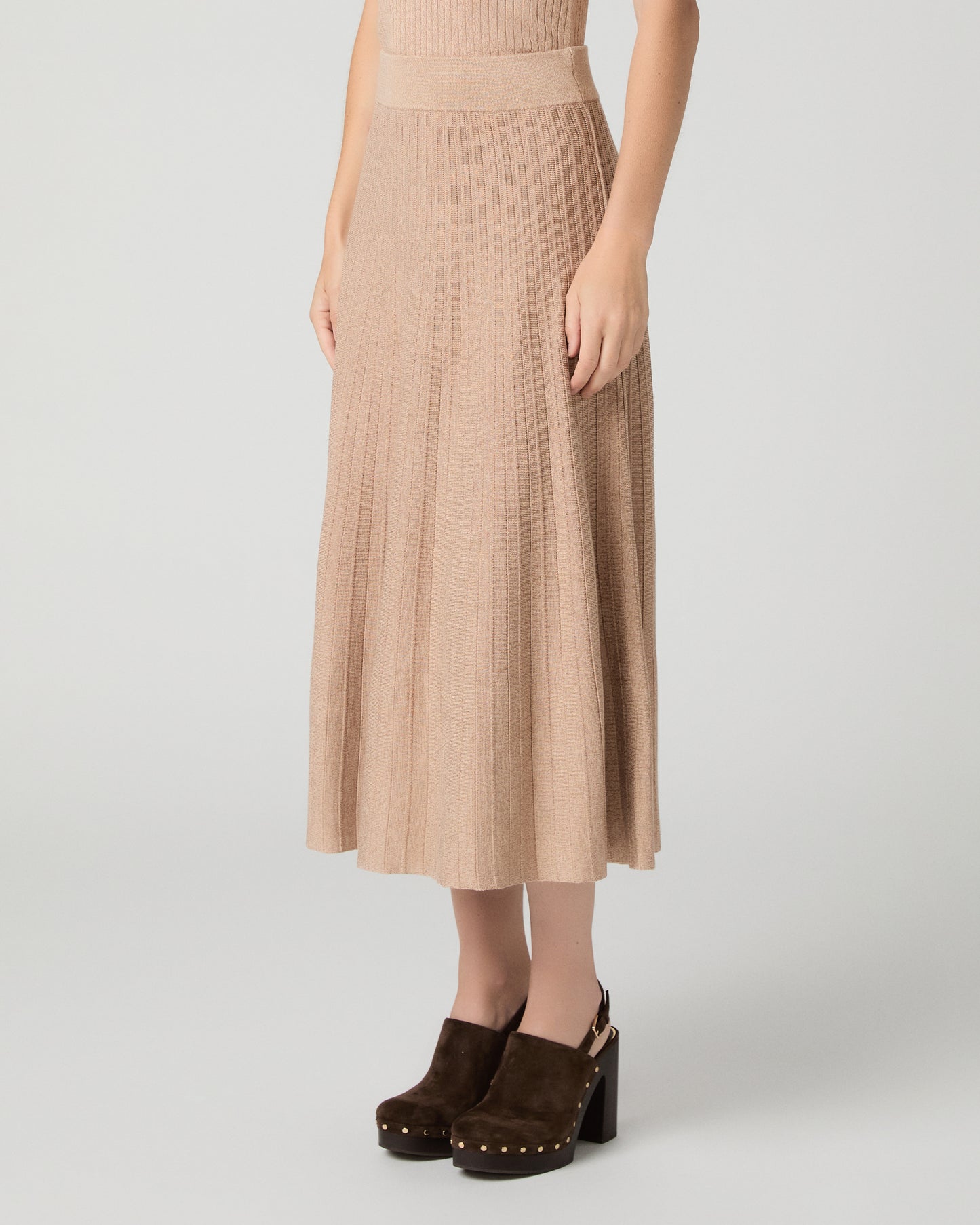 Women wearing a tan top and matching skirt paired with brown heels against a white background