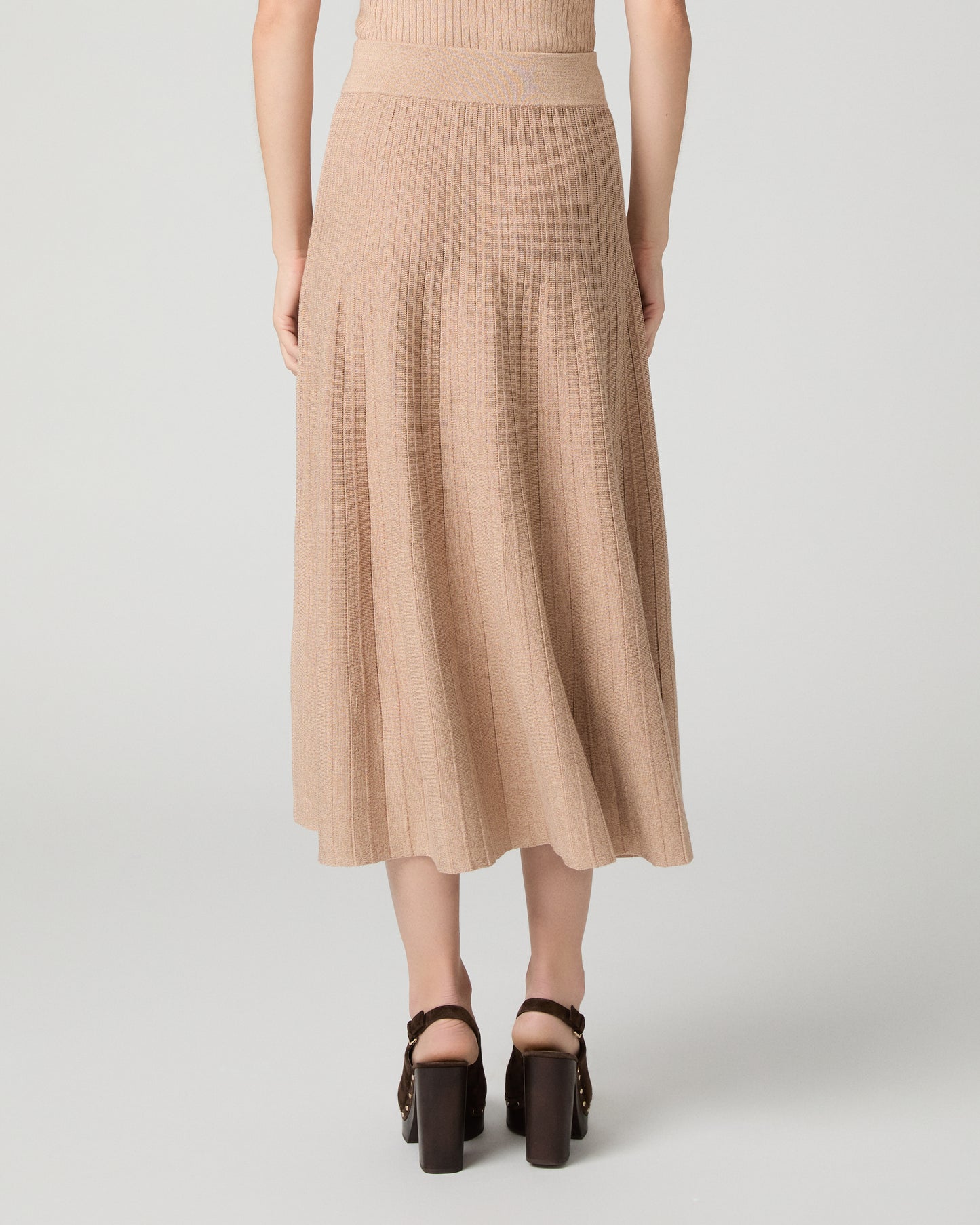 Women wearing a tan top and matching skirt paired with brown heels against a white background