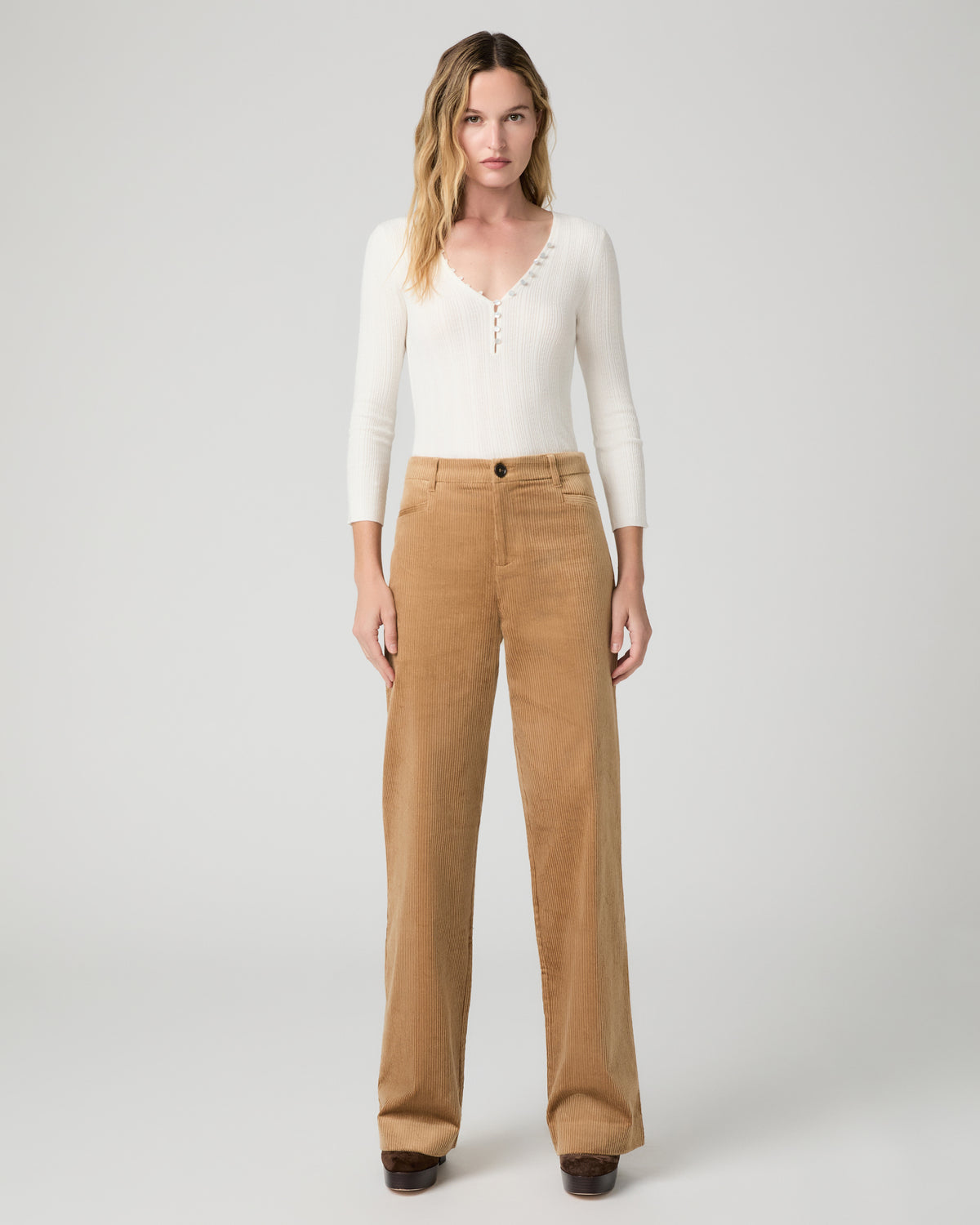 Women wearing a white long sleeve top paired with brown pants and brown boots against a white background