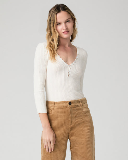 Women wearing a white long sleeve top paired with brown pants against a white background