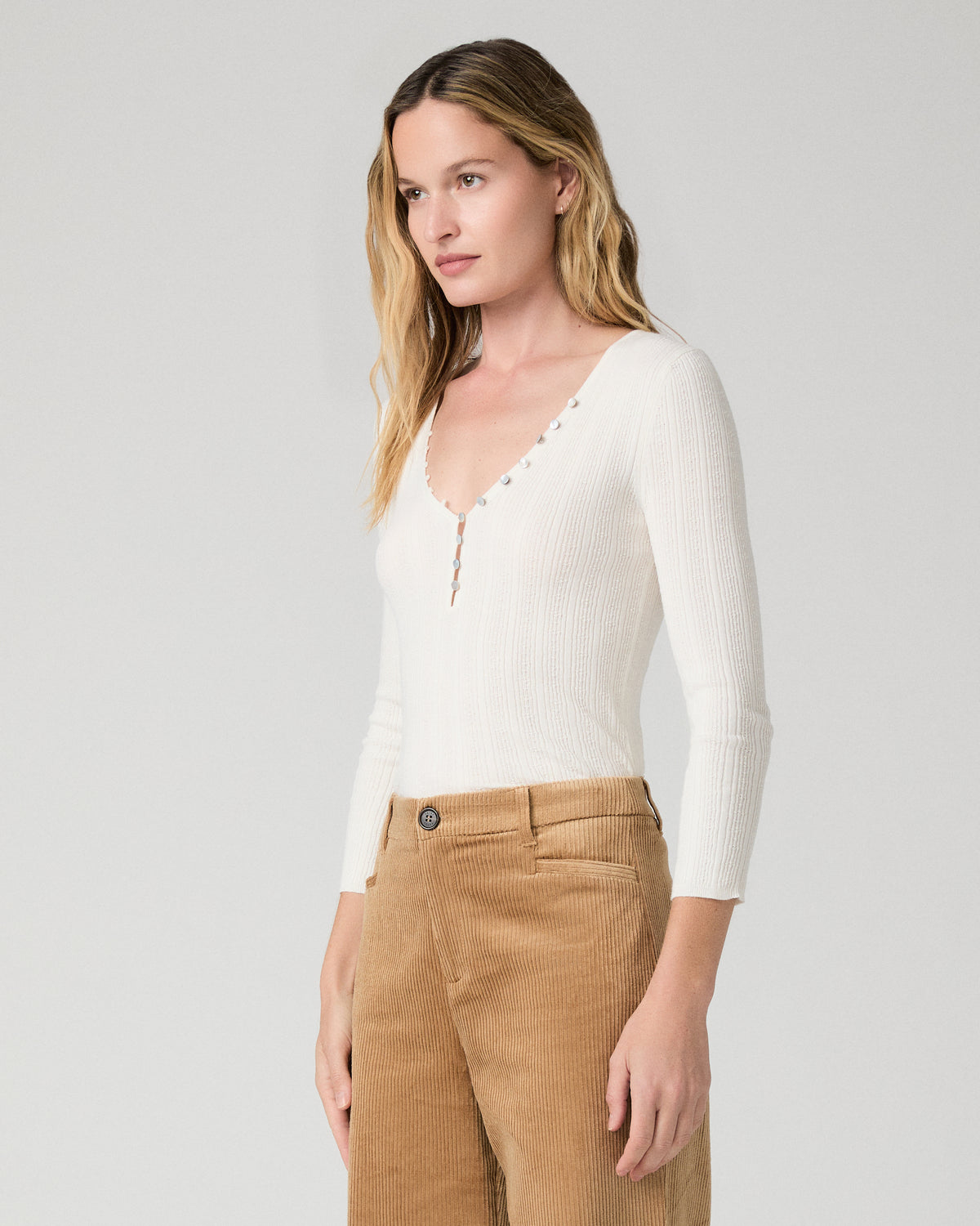 Women wearing a white long sleeve top paired with brown pants against a white background