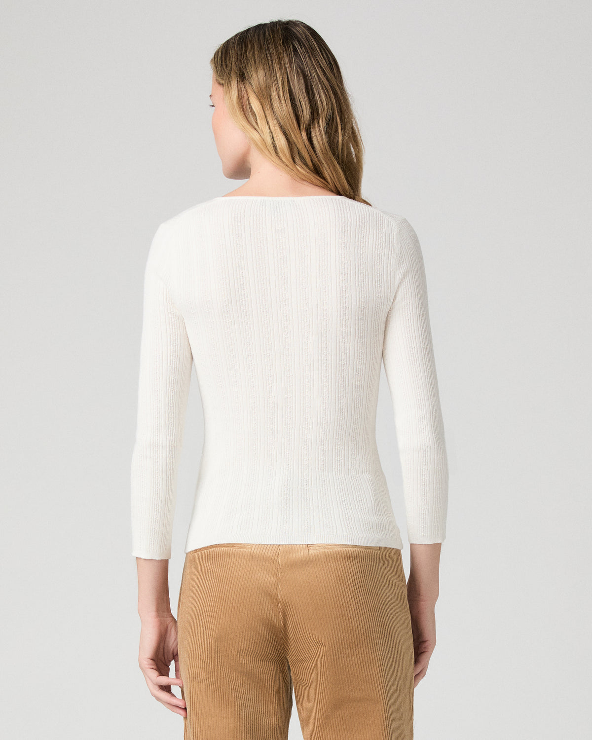 Women wearing a white long sleeve top paired with brown pants against a white background