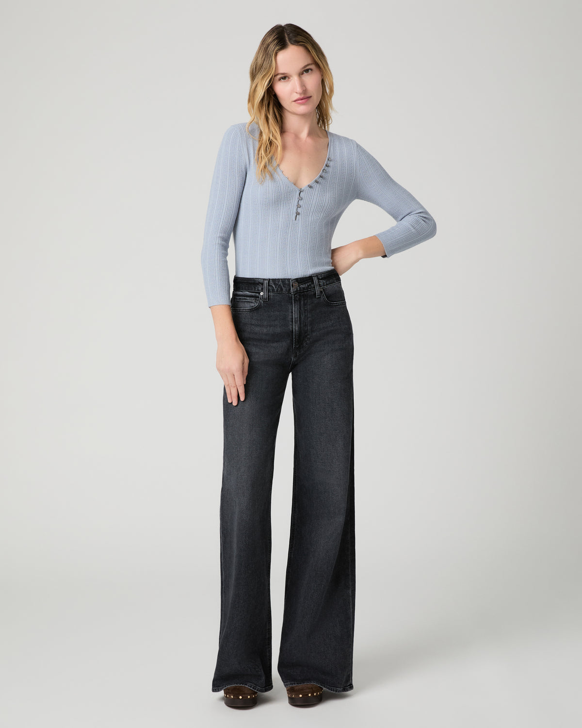 Women wearing a light blue top paired with black jeans and brown boots against a white background
