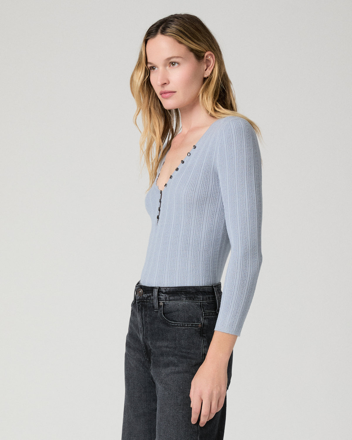 Women wearing a light blue top paired with black jeans against a white background