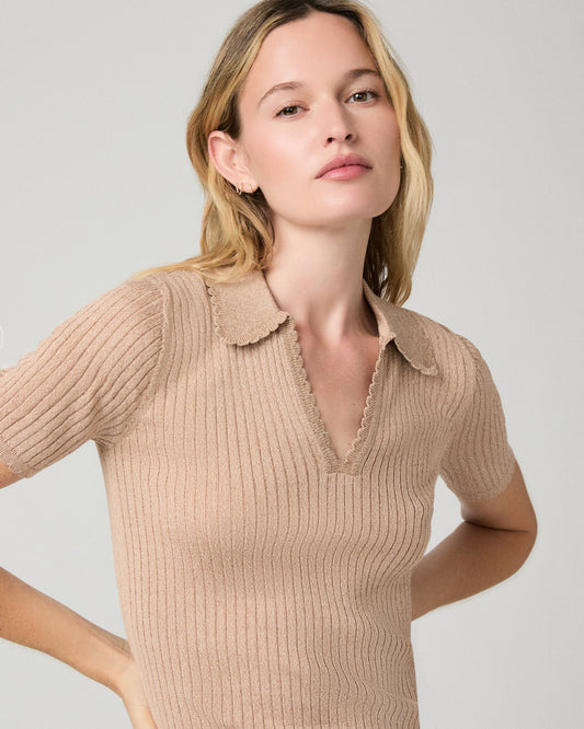A woman wearing a beige ribbed short-sleeve knit polo-style top with a scalloped V-neck collar, photographed against a light gray studio background.